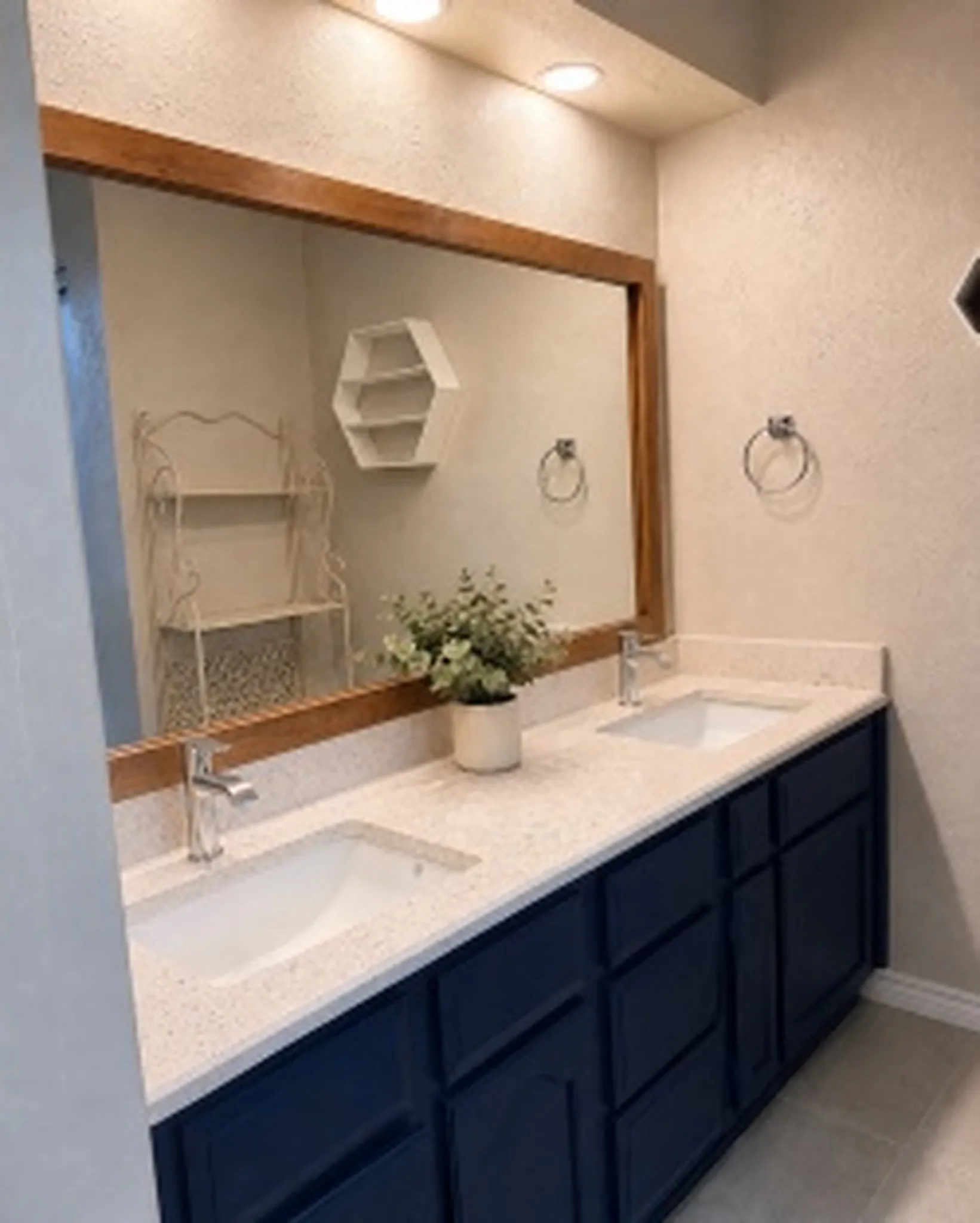 Primary - Dual undermount sinks with chrome faucets, a quartz countertop, and a wood-framed mirror