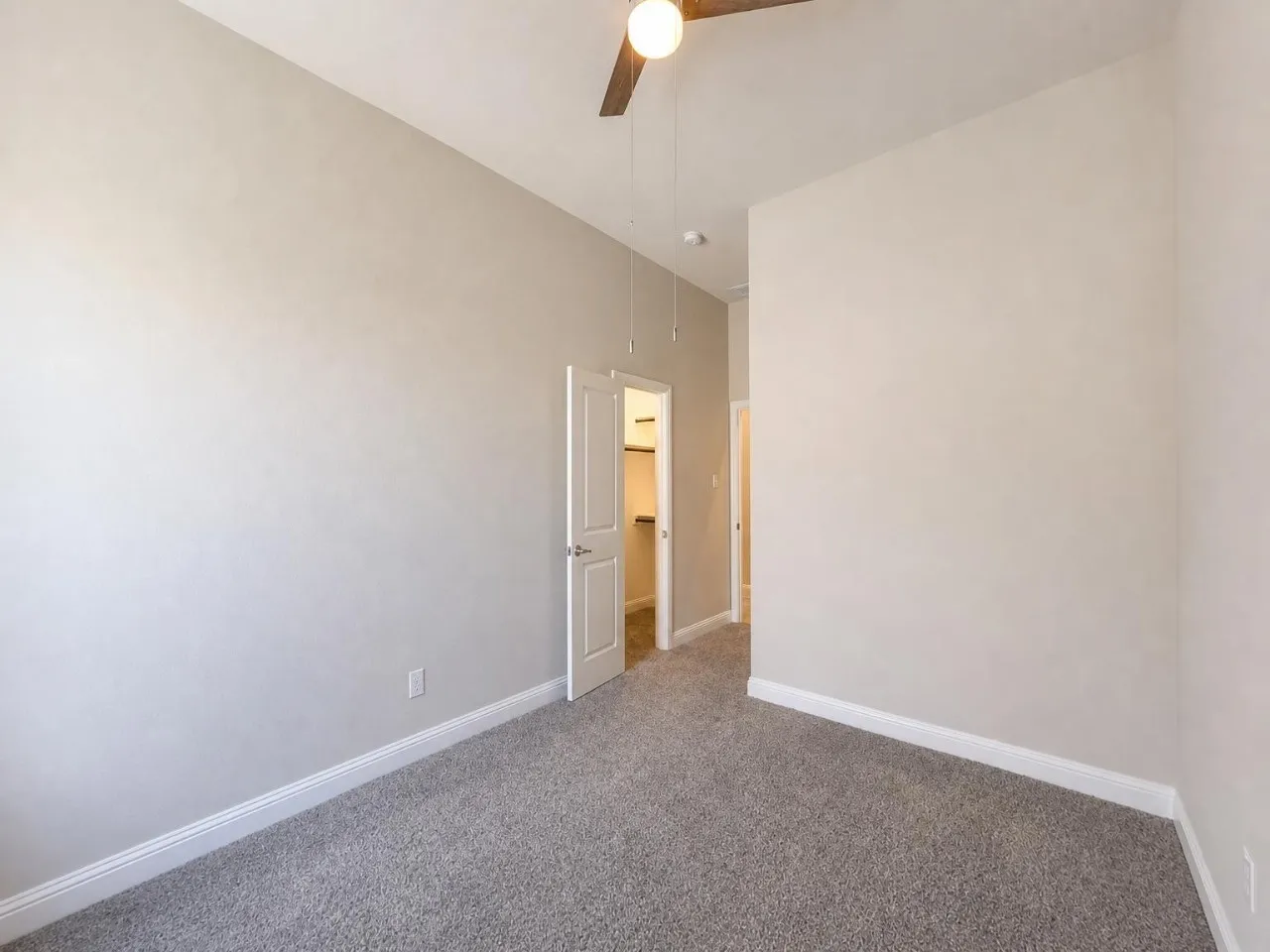 Sloped ceiling, ceiling fan, neutral wall paint, gray carpet, and white trim