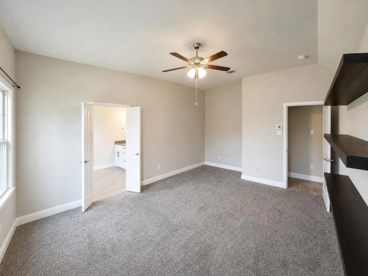 Carpeted room with a vaulted ceiling, ceiling fan, window, and built-in shelving