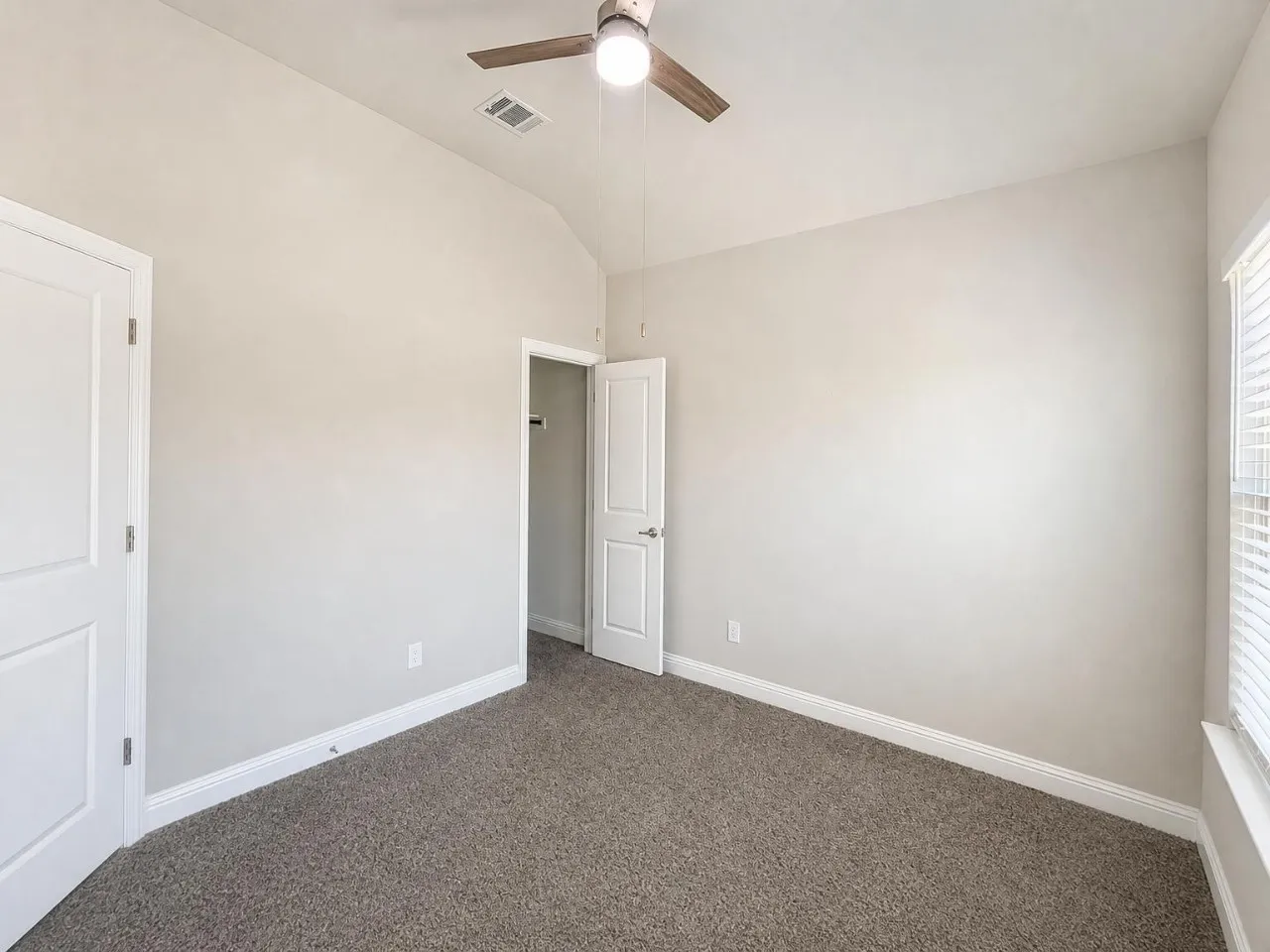 Vaulted ceiling, ceiling fan, white paneled doors, window with blinds, and neutral carpet flooring