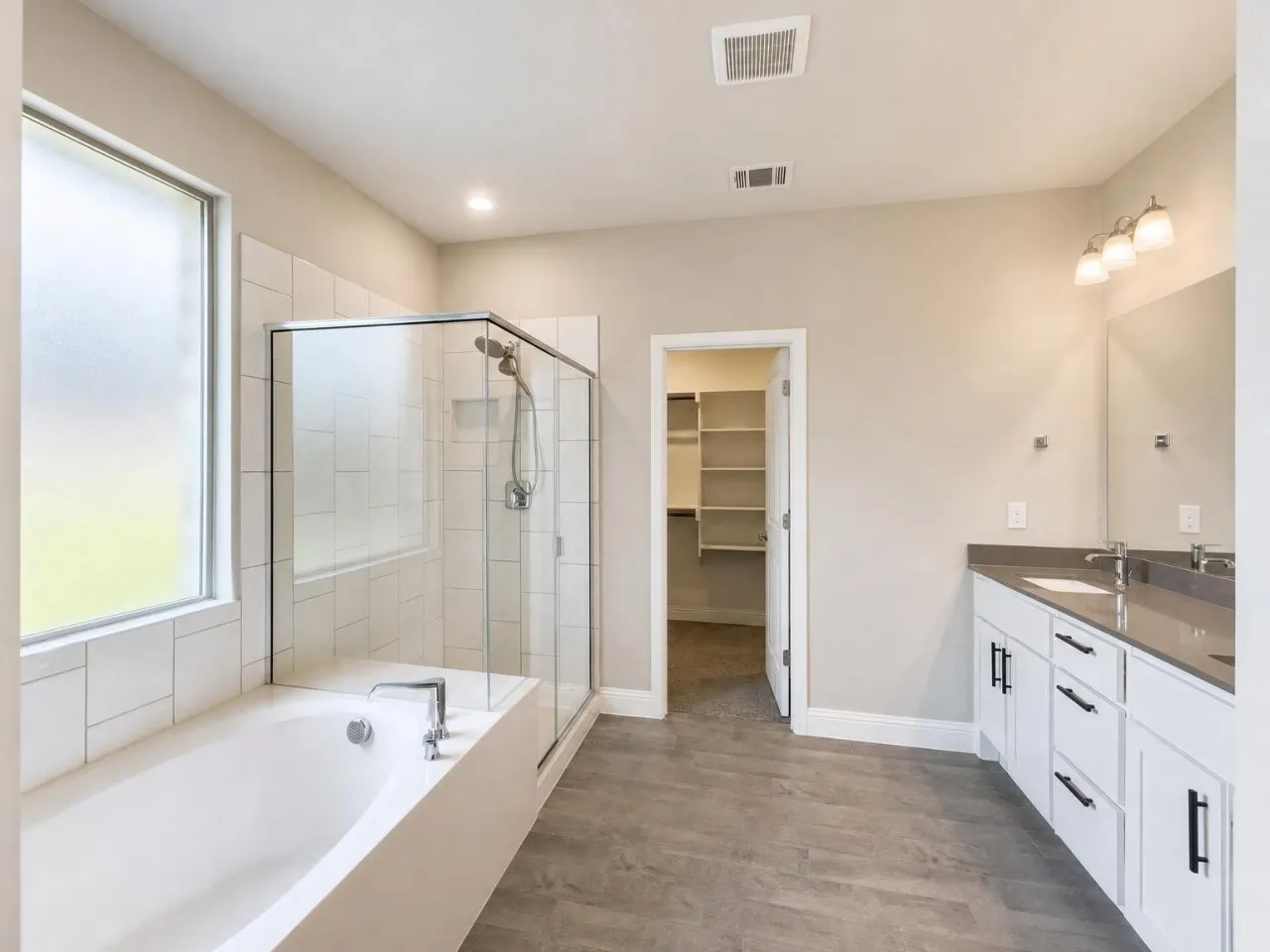 Spacious bathroom featuring a built-in bathtub, glass-enclosed shower, dual vanity with undermount sinks, and wood-finish flooring