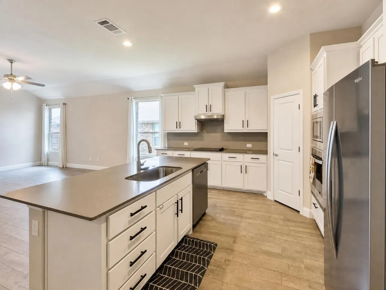 Kitchen featuring a central island with an undermount sink, stainless steel appliances, white cabinetry, and wood-finish flooring