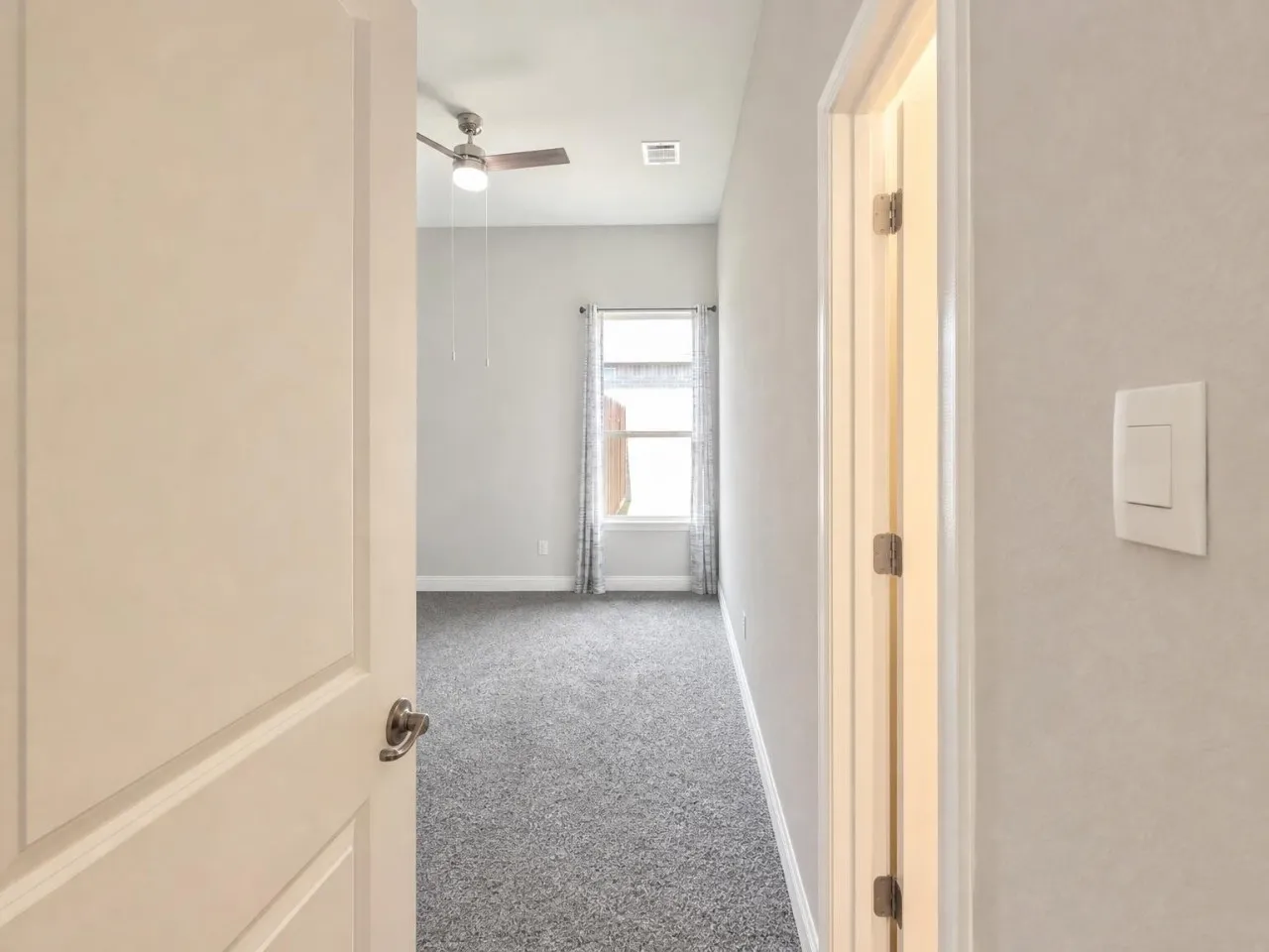 Room featuring textured carpet flooring, a ceiling fan with integrated lighting, and a single window with curtain rods