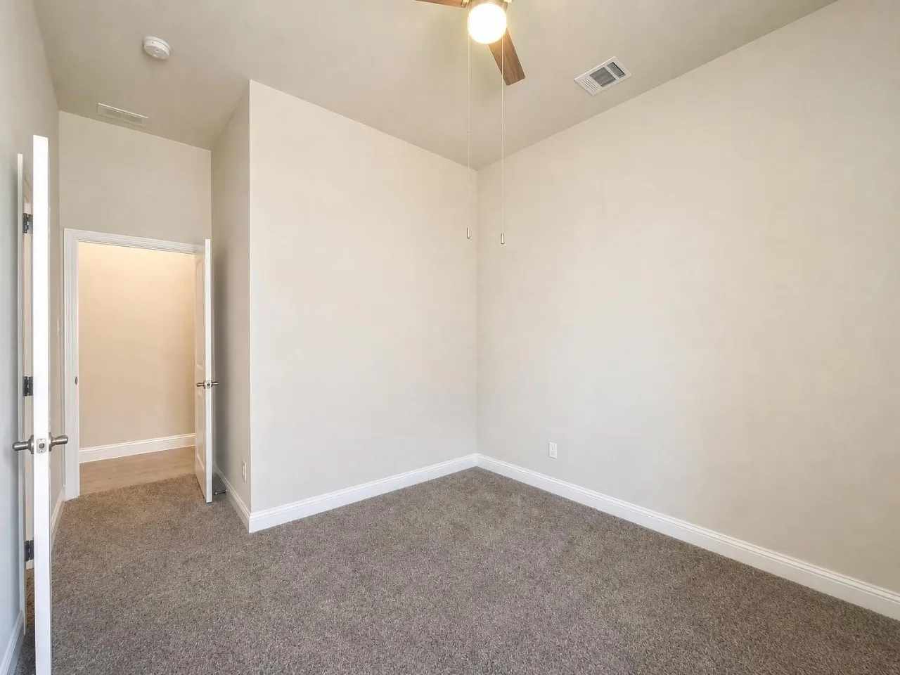 Neutral wall paint, ceiling fan with light fixture, gray carpet flooring, white trim, and a white interior door with a silver handle