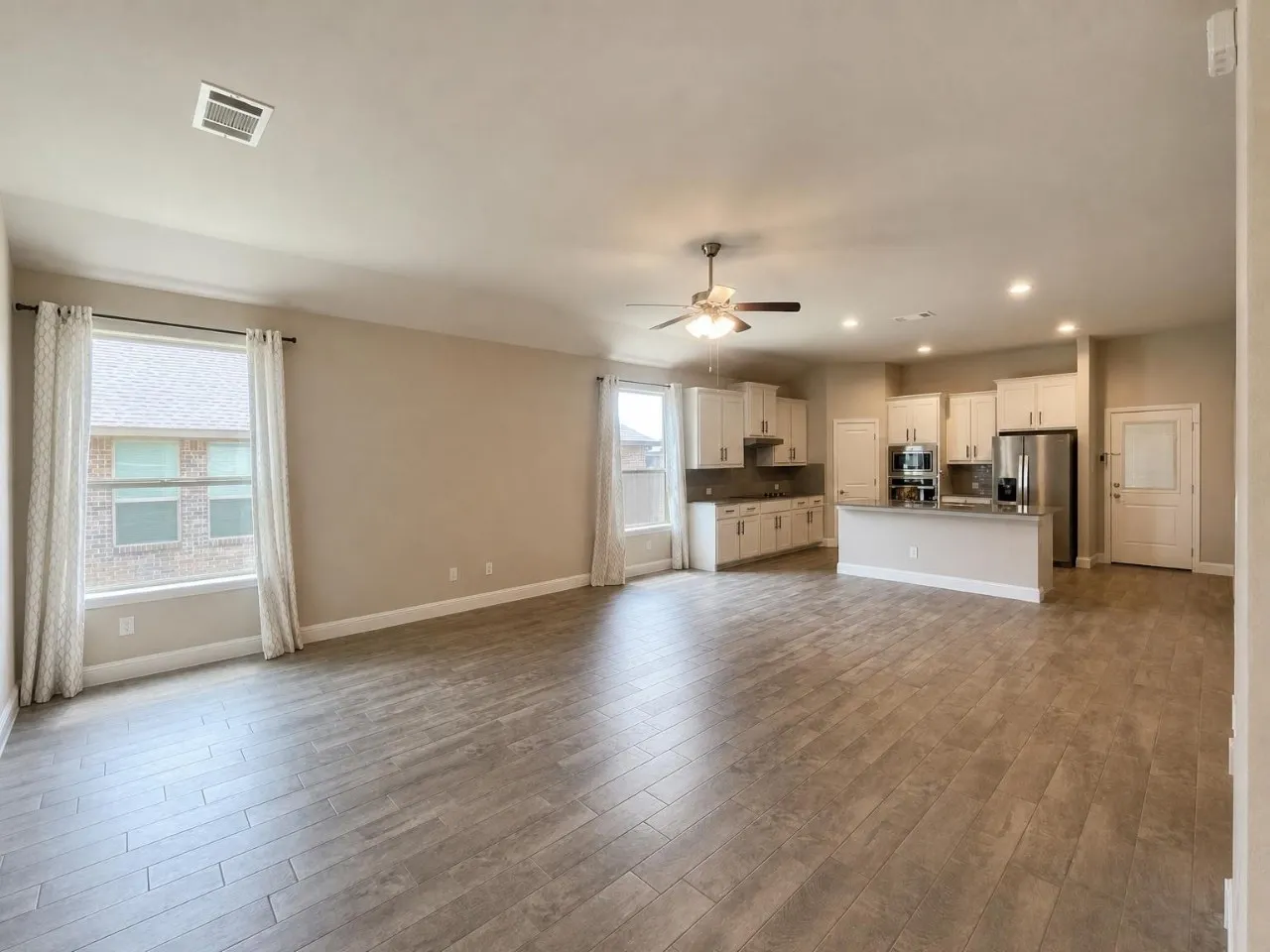 Spacious open-concept living area featuring wood-look tile flooring, white kitchen cabinetry, stainless steel appliances, a kitchen island, and recessed lighting