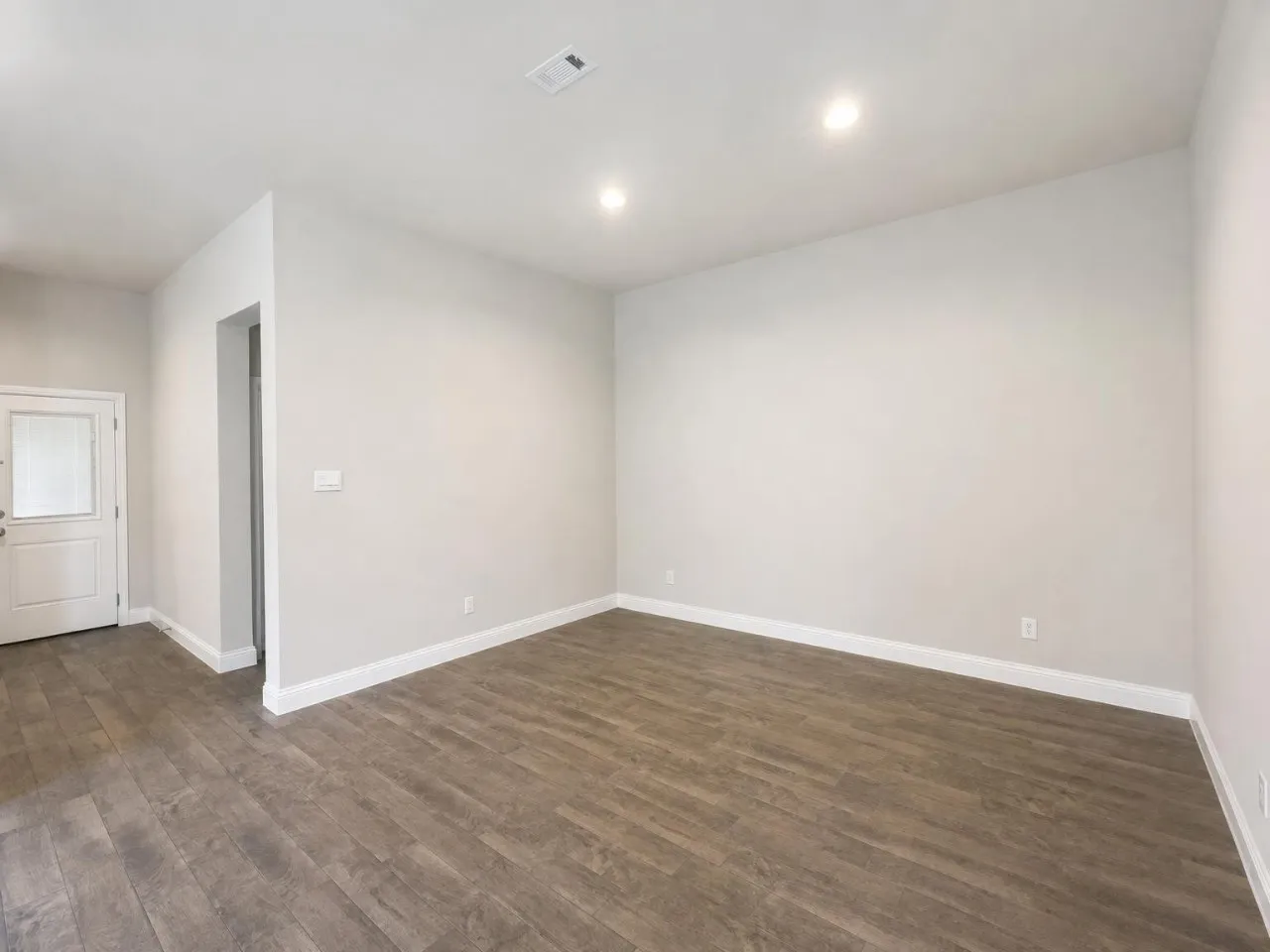 Recessed lighting illuminates the wood-finish flooring and light-toned walls