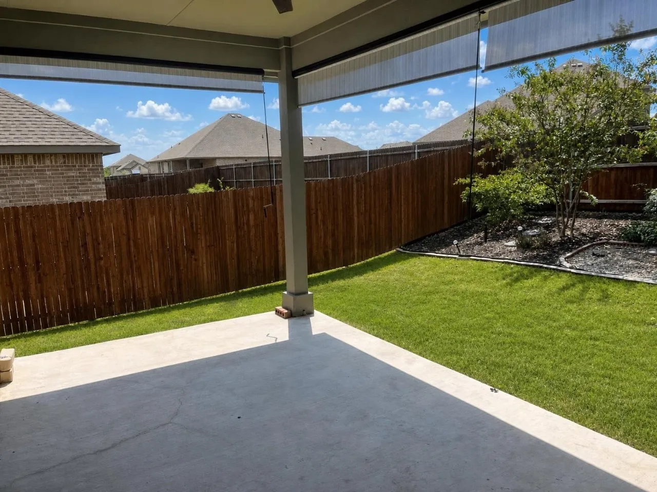 Covered concrete patio, expansive lawn, wood privacy fencing, and established landscaping