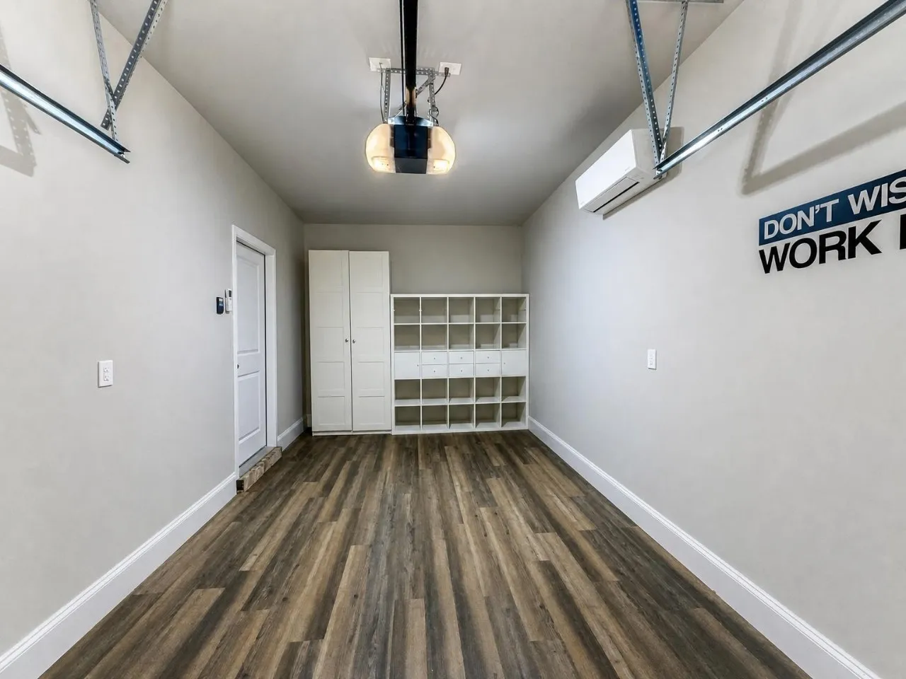 Wood-finish flooring, built-in storage shelving, built-in storage cabinet, split-system air conditioning unit, and overhead garage door opener