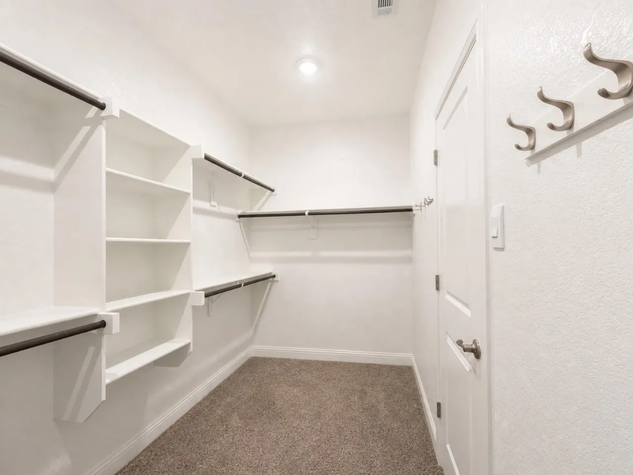 Walk-in closet featuring white built-in shelving, multiple hanging rods, and carpet flooring