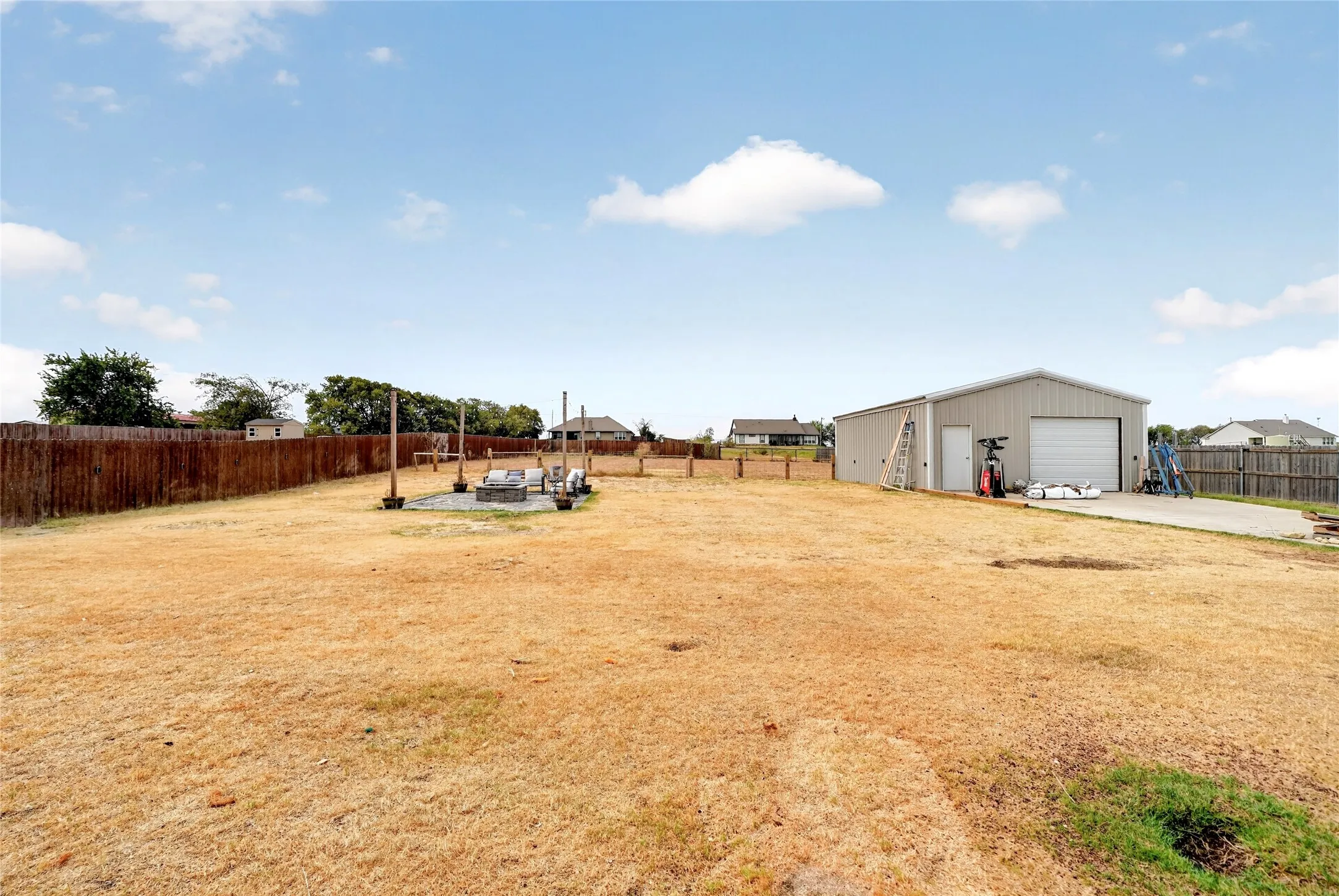 Detached metal building with overhead door and side entry, concrete pad, wood privacy fencing, and an outdoor patio area