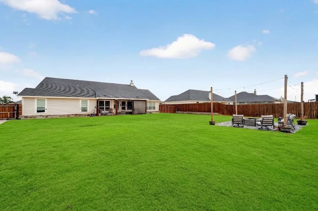 Expansive backyard featuring a lush green lawn, covered patio, privacy fencing, and a dedicated fire pit area