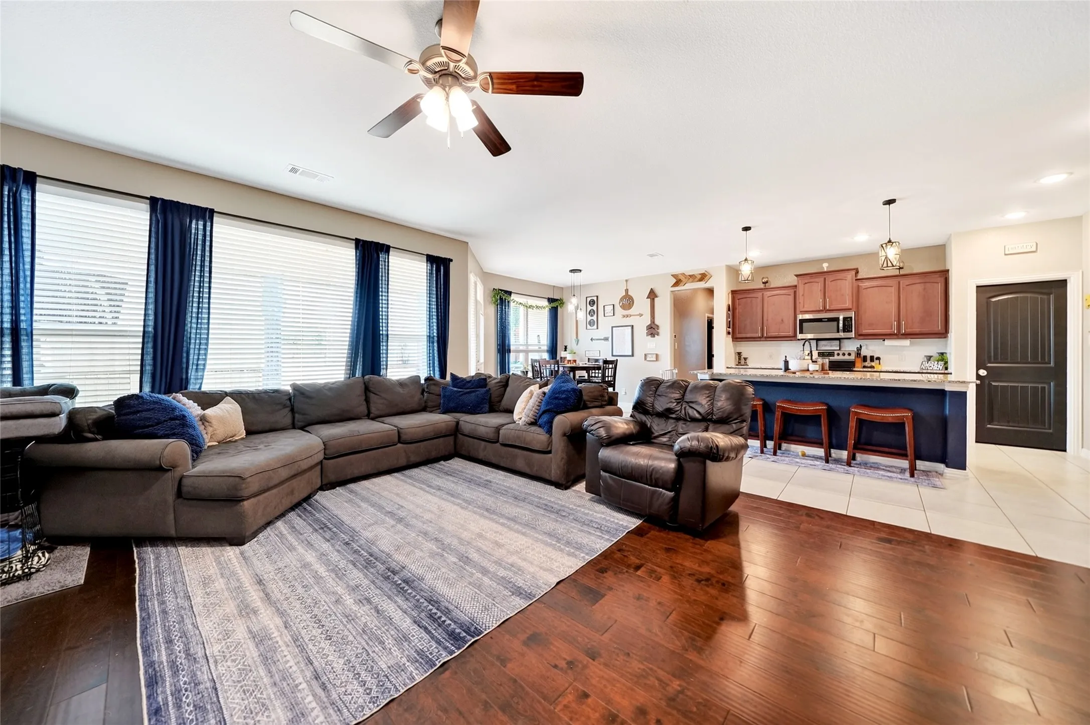 Hardwood flooring, kitchen island with seating, stainless steel appliances, pendant lighting, and ceiling fan