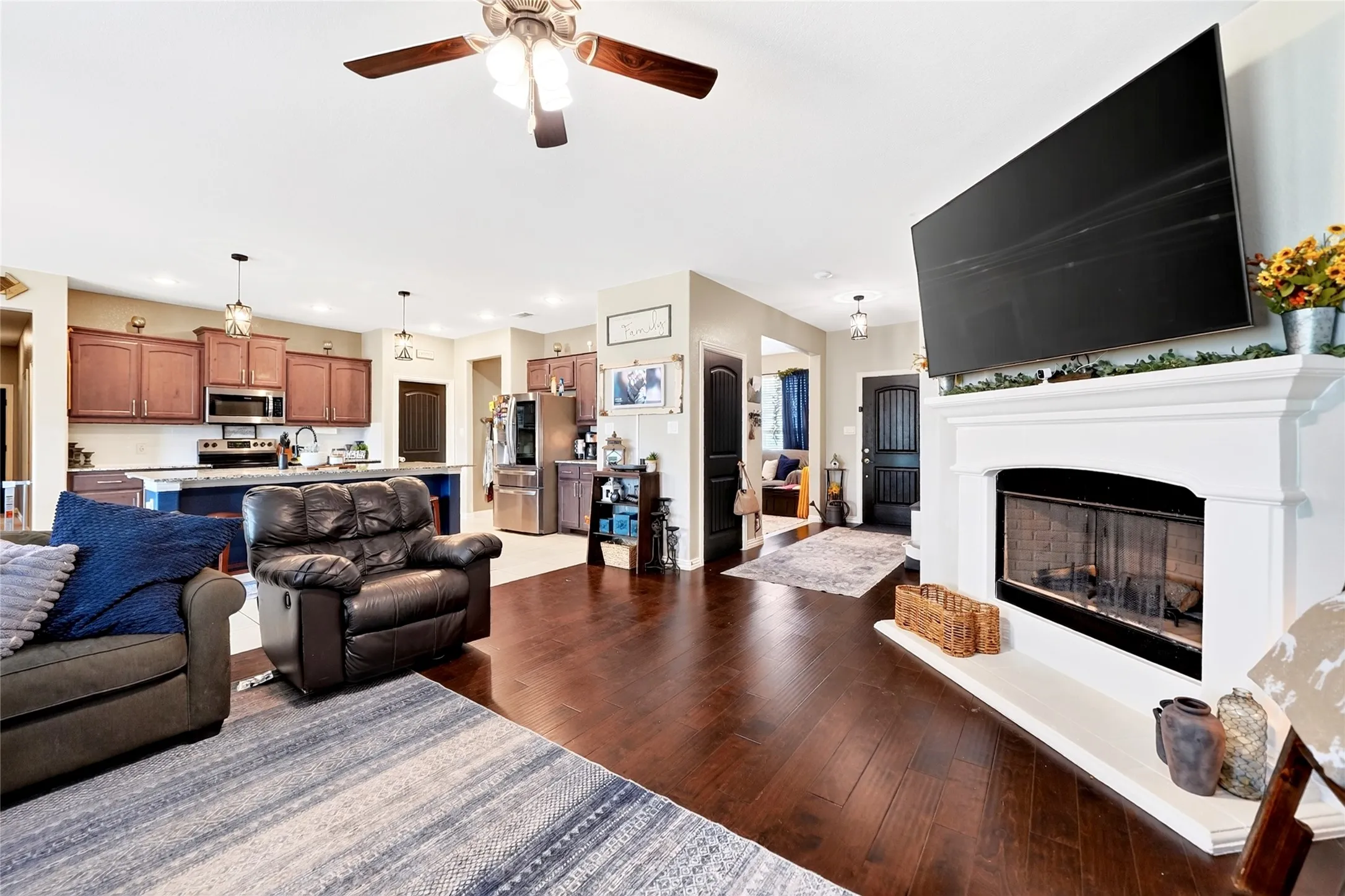 Open-concept living area with dark wood-finish flooring, a white mantel fireplace, and a ceiling fan