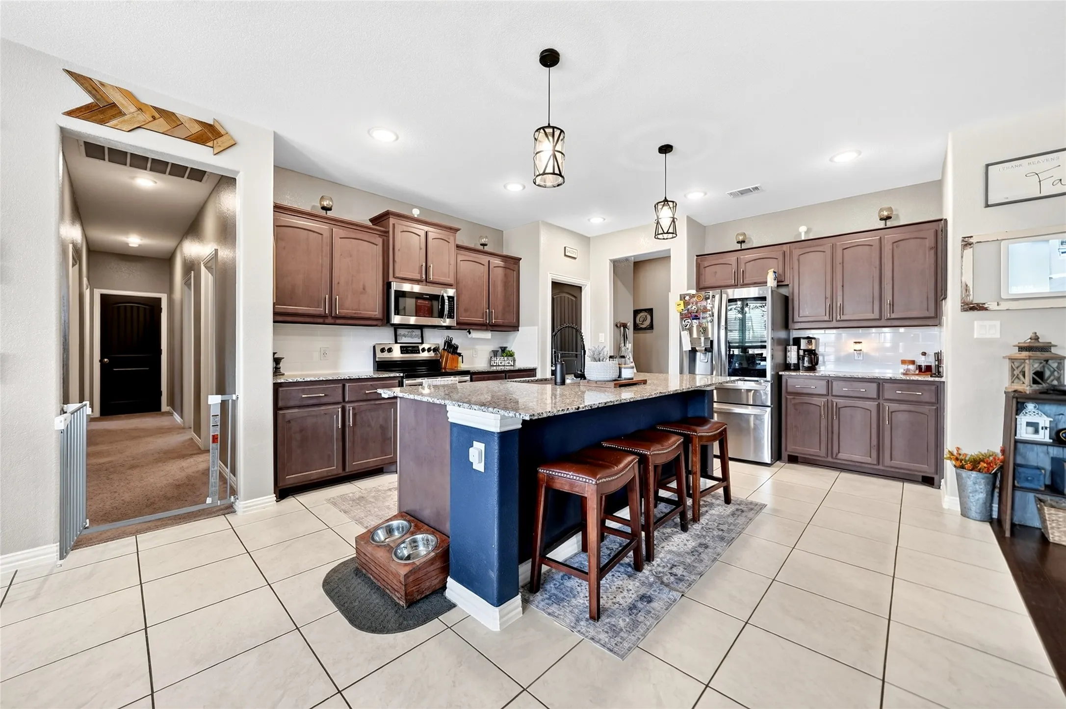 Spacious kitchen featuring an expansive center island with seating, stainless steel appliances, dark wood cabinetry, light tile flooring, and recessed lighting