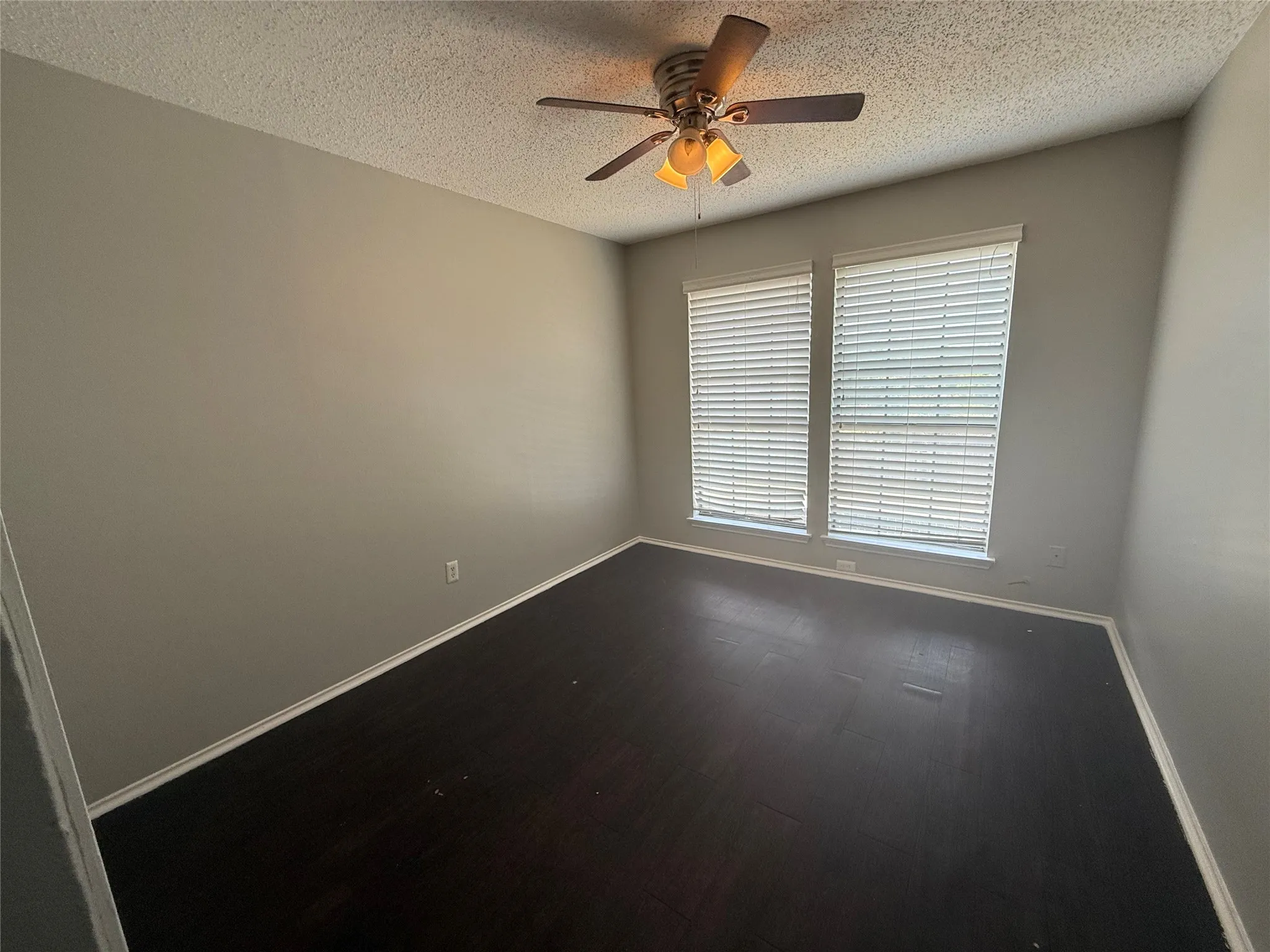 Dark wood-finish flooring with white trim, neutral wall color, and a ceiling fan with integrated lighting