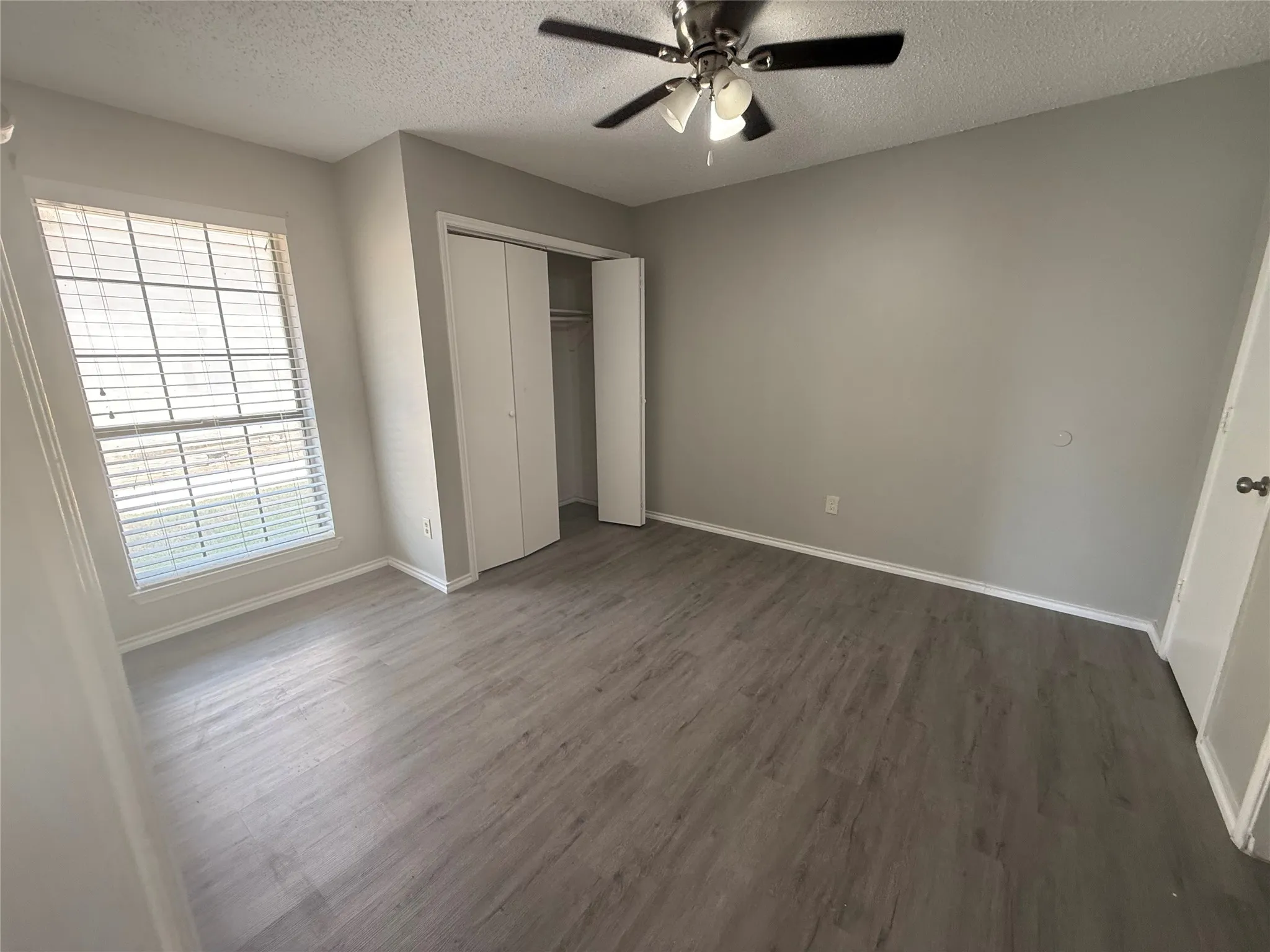 Spacious room featuring wood-finish flooring, a ceiling fan, window with blinds, and white bi-fold closet doors