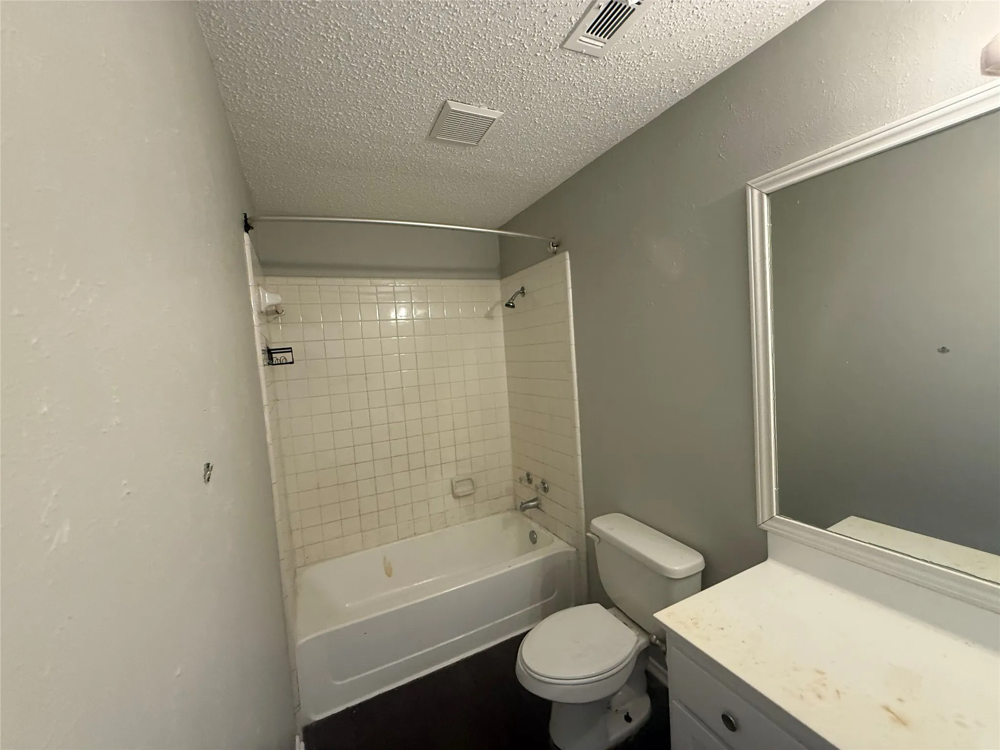 White subway tile tub surround, white vanity with integrated sink, framed wall mirror, and dark wood-finish flooring