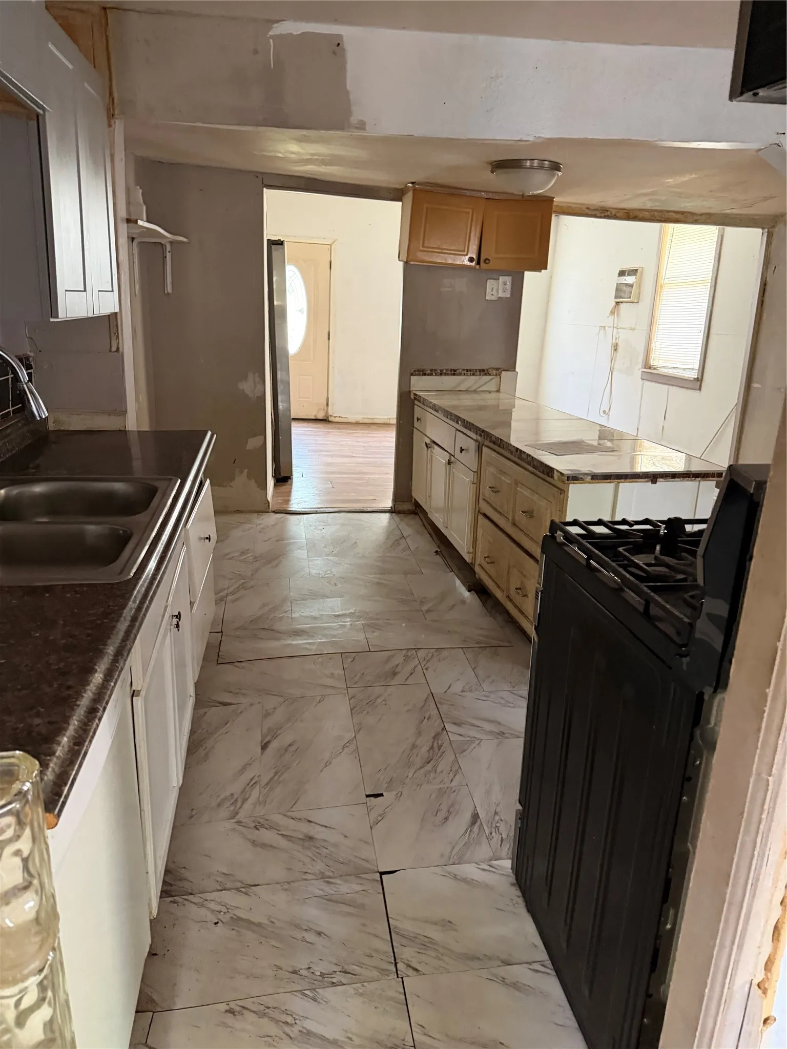 Kitchen featuring white cabinetry, a double basin stainless steel sink, a gas range, and light-toned tile flooring