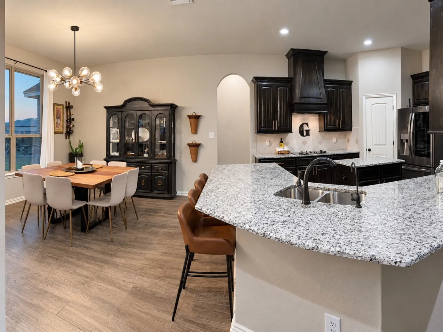 Spacious kitchen and dining area featuring wood-finish flooring, dark cabinetry, granite countertops, and a double basin sink
