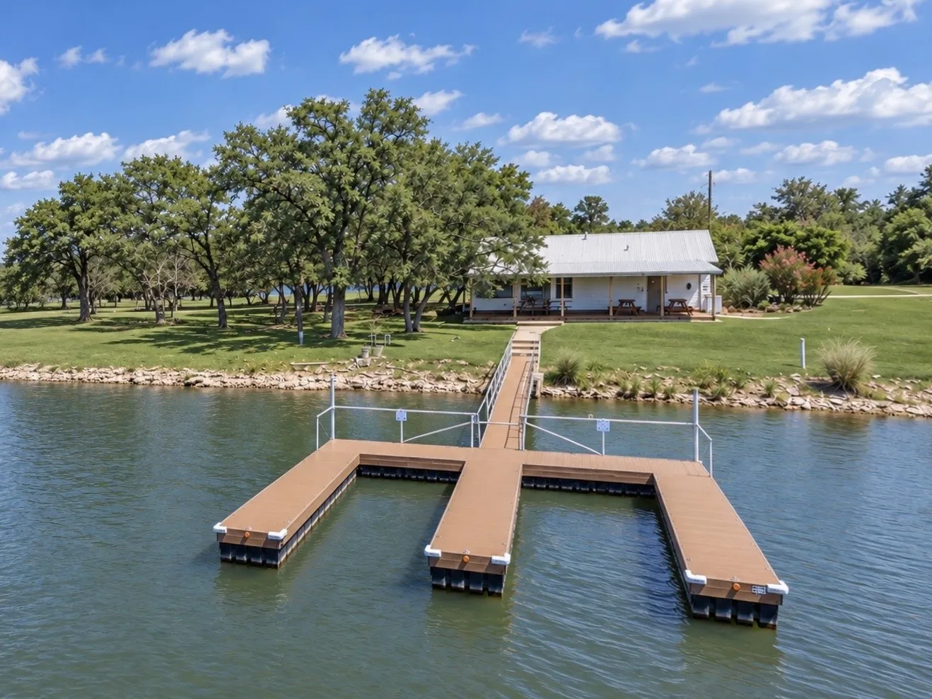 Waterfront property with a private dock featuring a multi-slip configuration, an extended gangway, a metal-roofed structure, and mature trees