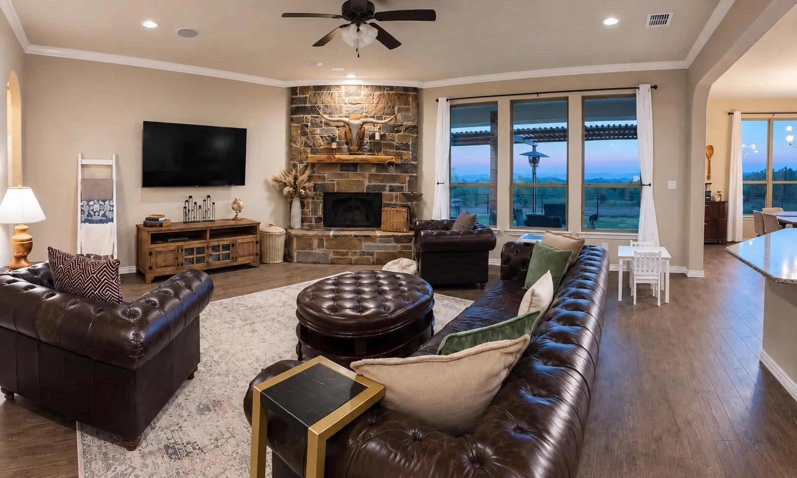 Spacious living area featuring a stone-clad fireplace with a wood mantel, wood-finish flooring, and expansive windows