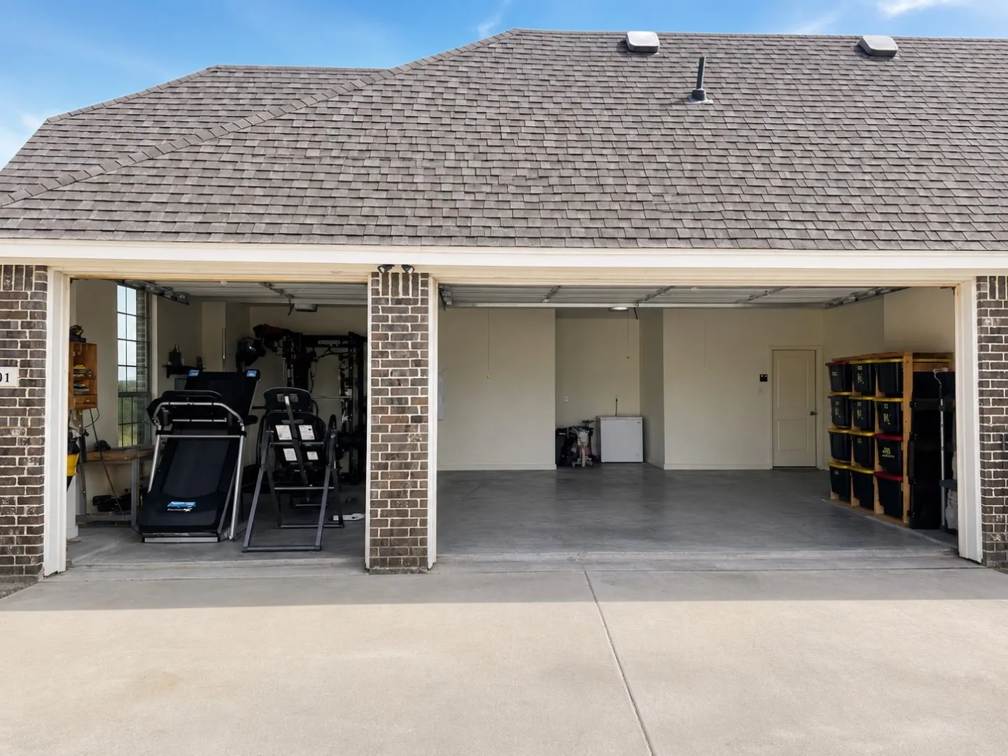 Multi-bay garage with concrete flooring, brick columns, and a shingled roof