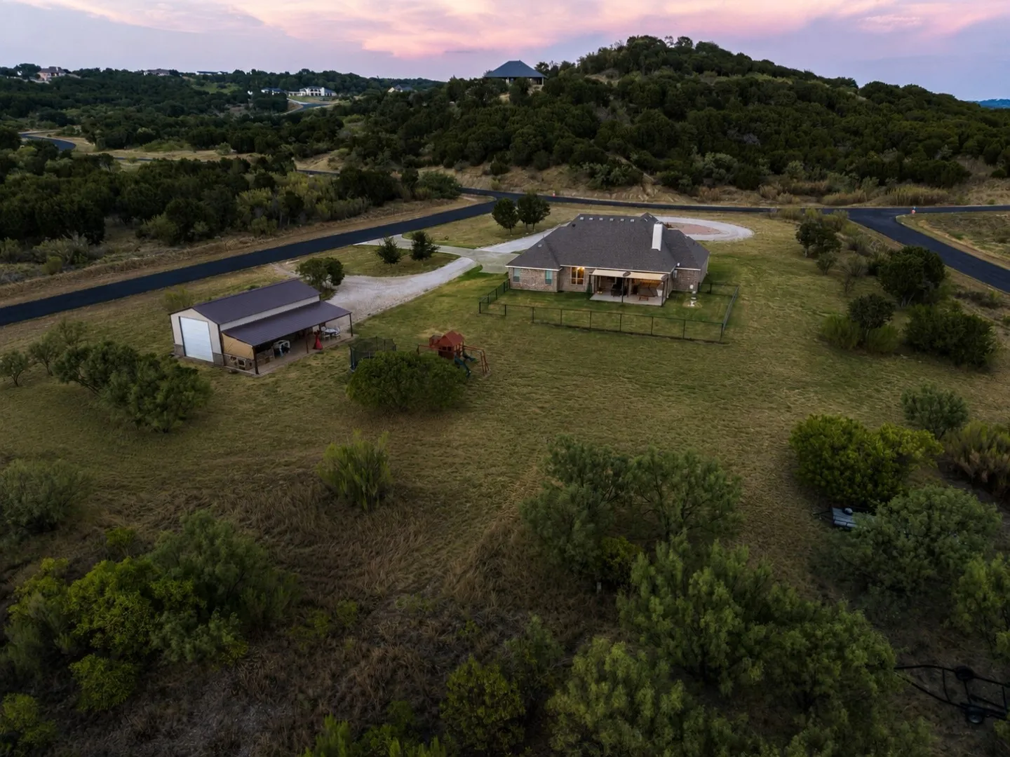 Expansive property featuring a single-story residence, separate metal outbuilding, covered patio, surrounding natural landscape, and paved driveway access
