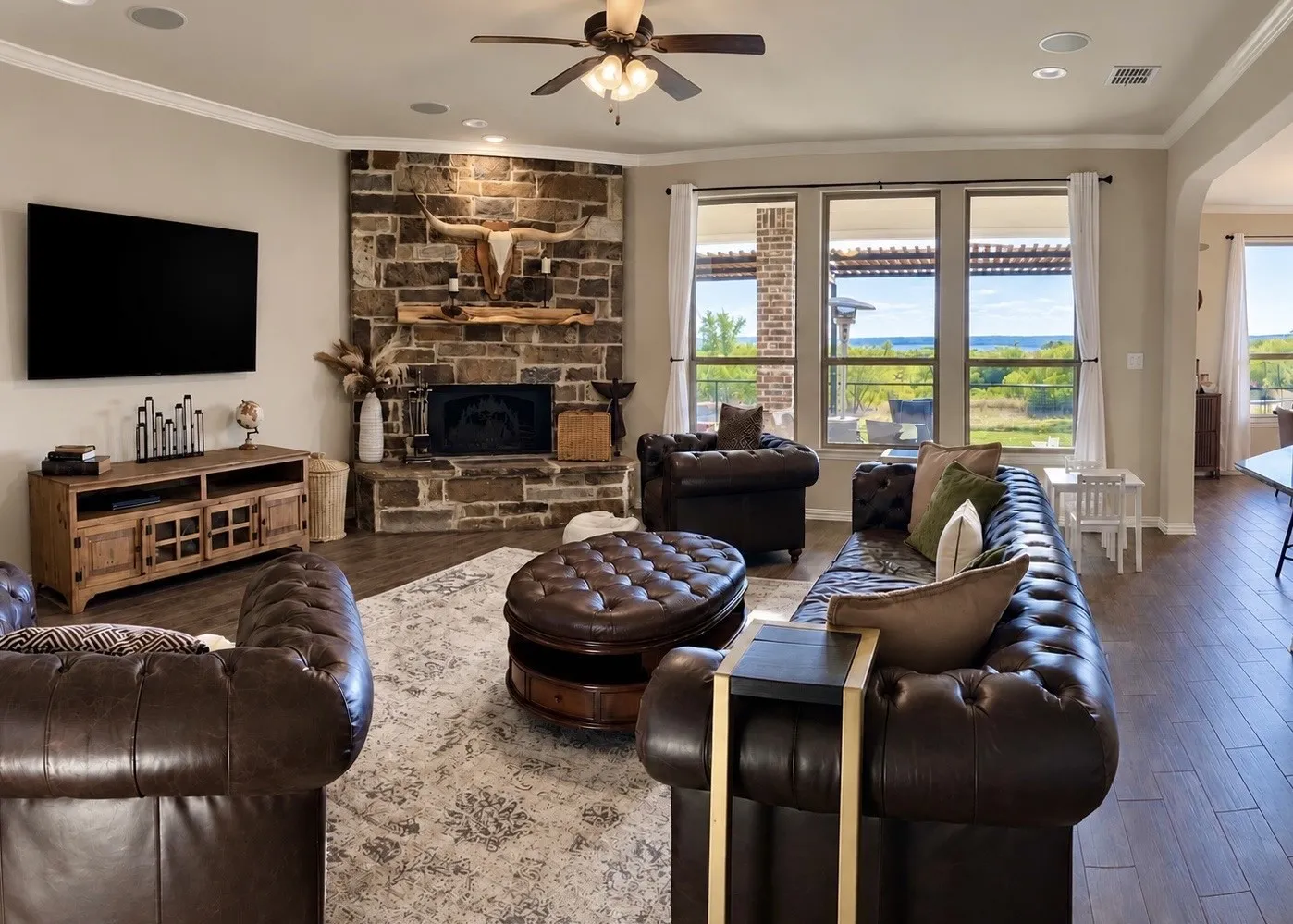 Stone-clad fireplace with hearth, wood-finish flooring, ceiling fan, recessed lighting, and multiple windows