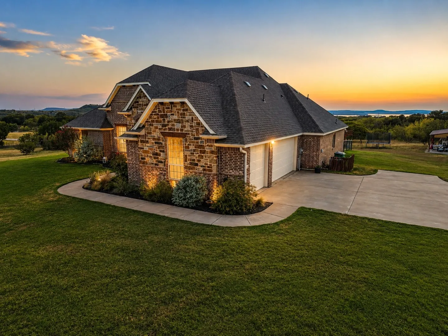 Stone and brick facade, multi-gabled roofline, concrete driveway, attached garage, and mature landscaping