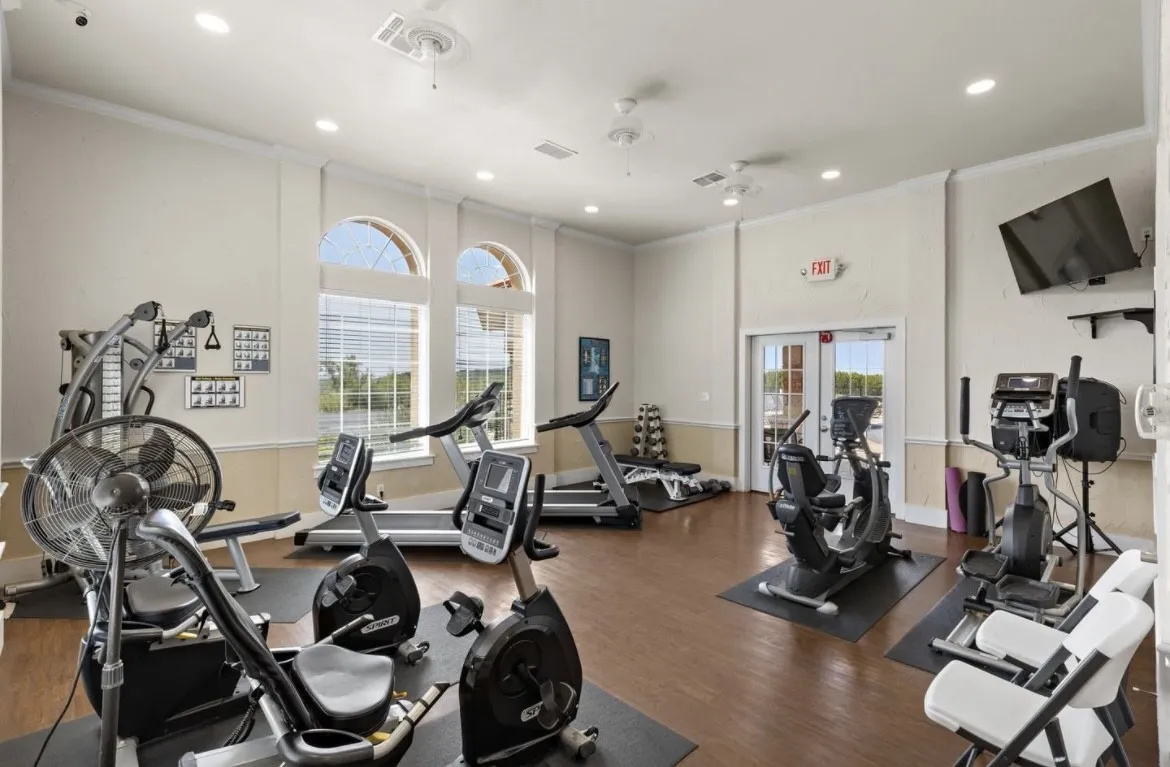 Spacious exercise room featuring wood-finish flooring, two arched windows with blinds, recessed lighting, and ceiling fans
