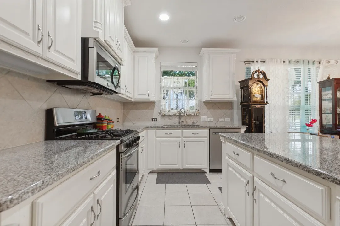 The roomy kitchen boasts white cabinetry, granite countertops, tile flooring, stainless steel appliances, and a tile backsplash!