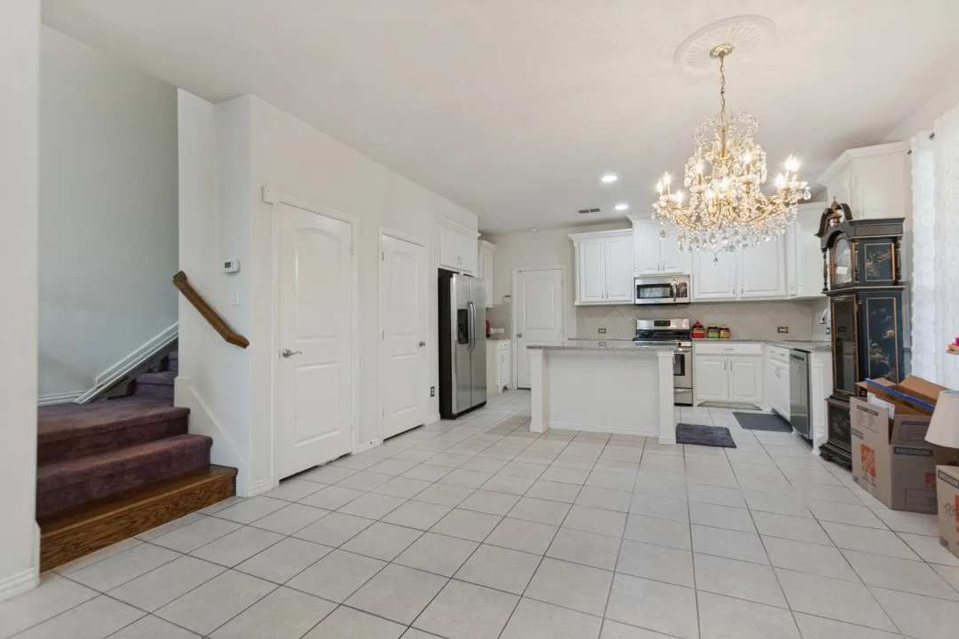 Spacious kitchen featuring elegant white cabinetry, modern stainless steel appliances, a functional center island with stone countertops, and durable tile flooring.