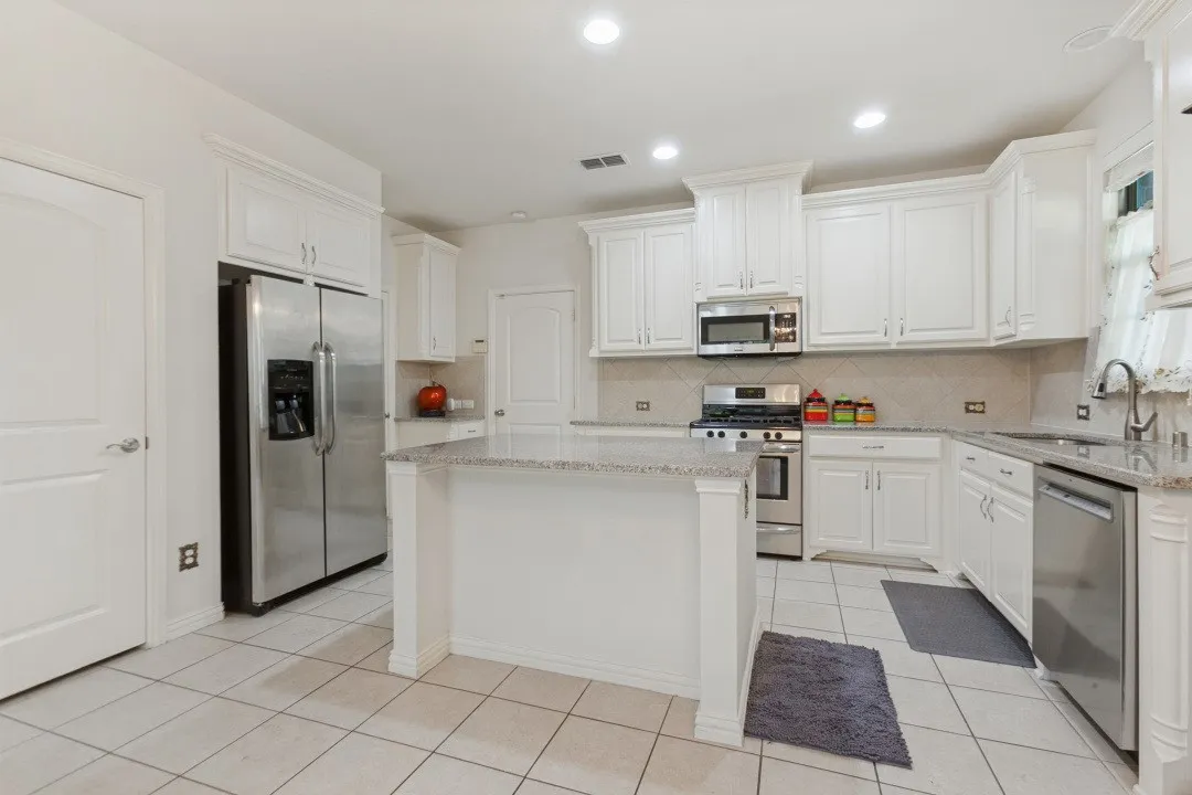 Gourmet kitchen with white cabinetry, granite island, and stainless steel appliances.