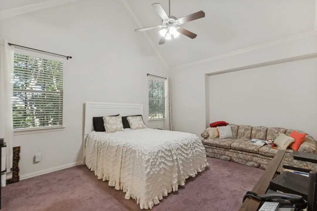 Primary Bedroom featuring a vaulted ceiling, ceiling fan, crown molding, double windows with blinds, and recessed space with enough room for a sitting area.