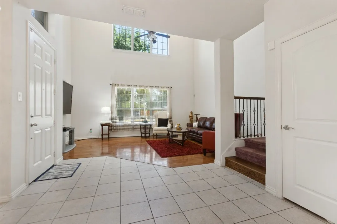 Vaulted ceilings, large windows, wood-finish flooring, tiled entry, and a staircase with wrought iron balusters