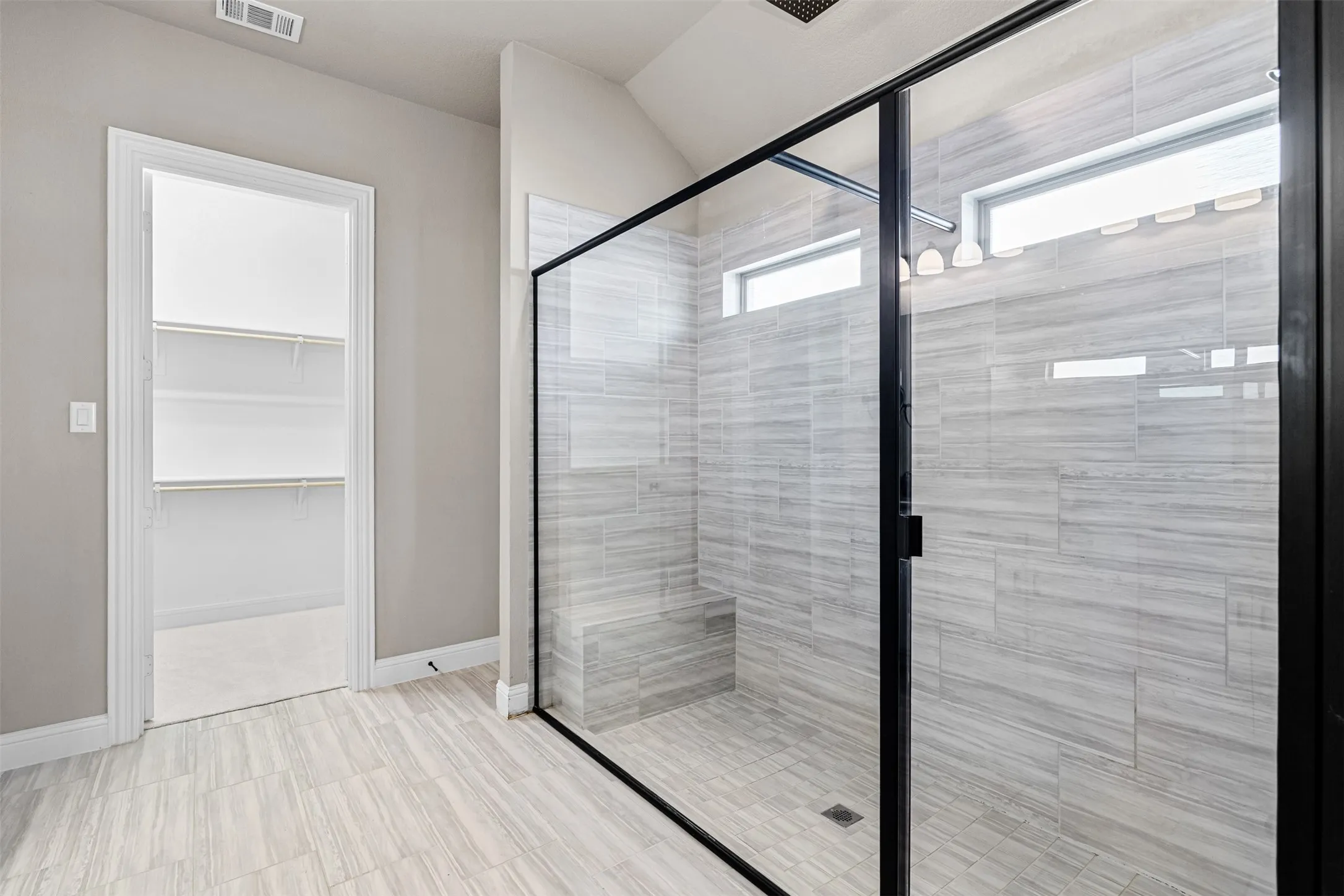 Glass-enclosed shower with black framing, tiled walls, and a built-in bench