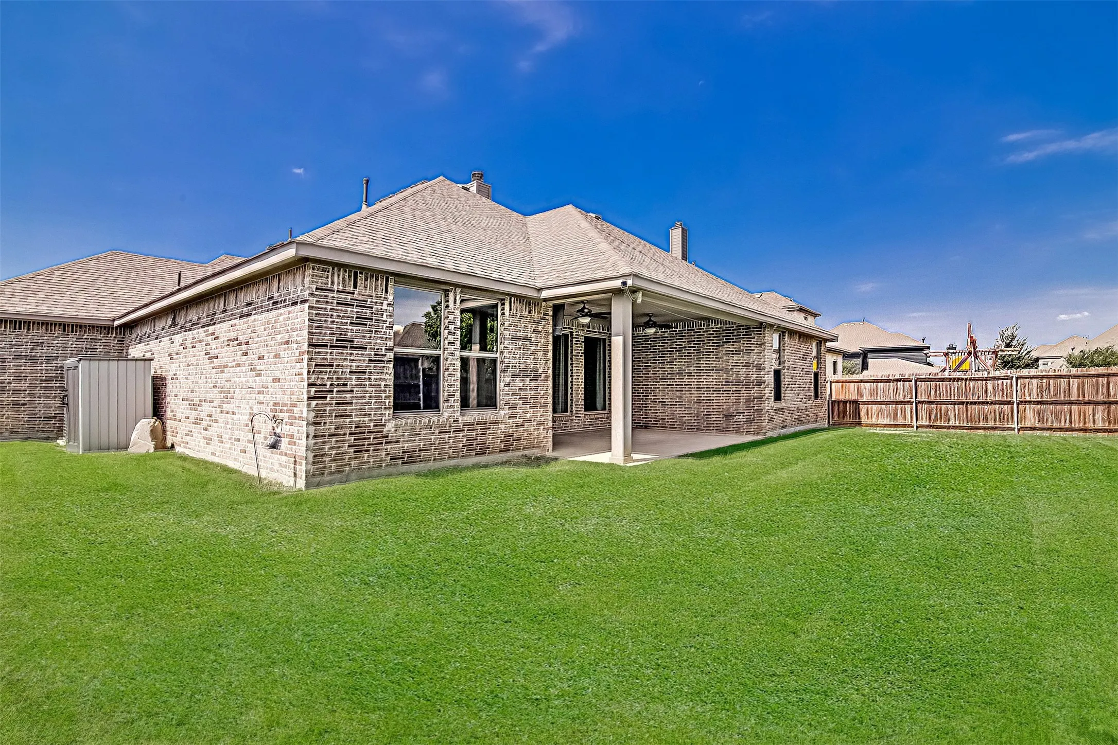 Expansive rear lawn with a covered patio, brick exterior, and multi-pane windows