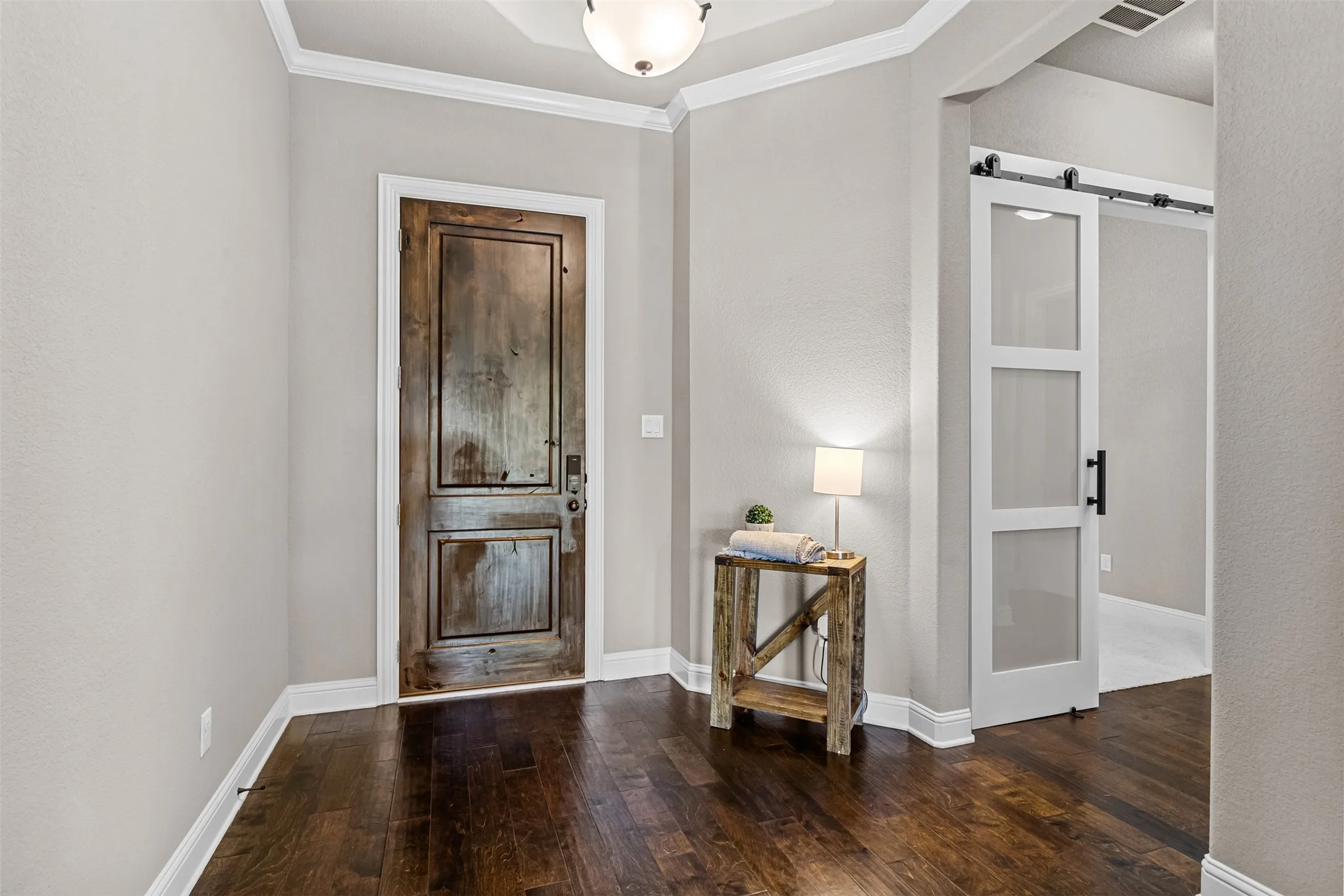 Hardwood flooring, crown molding, a rustic-finish entry door, and a modern sliding barn door with frosted glass panels