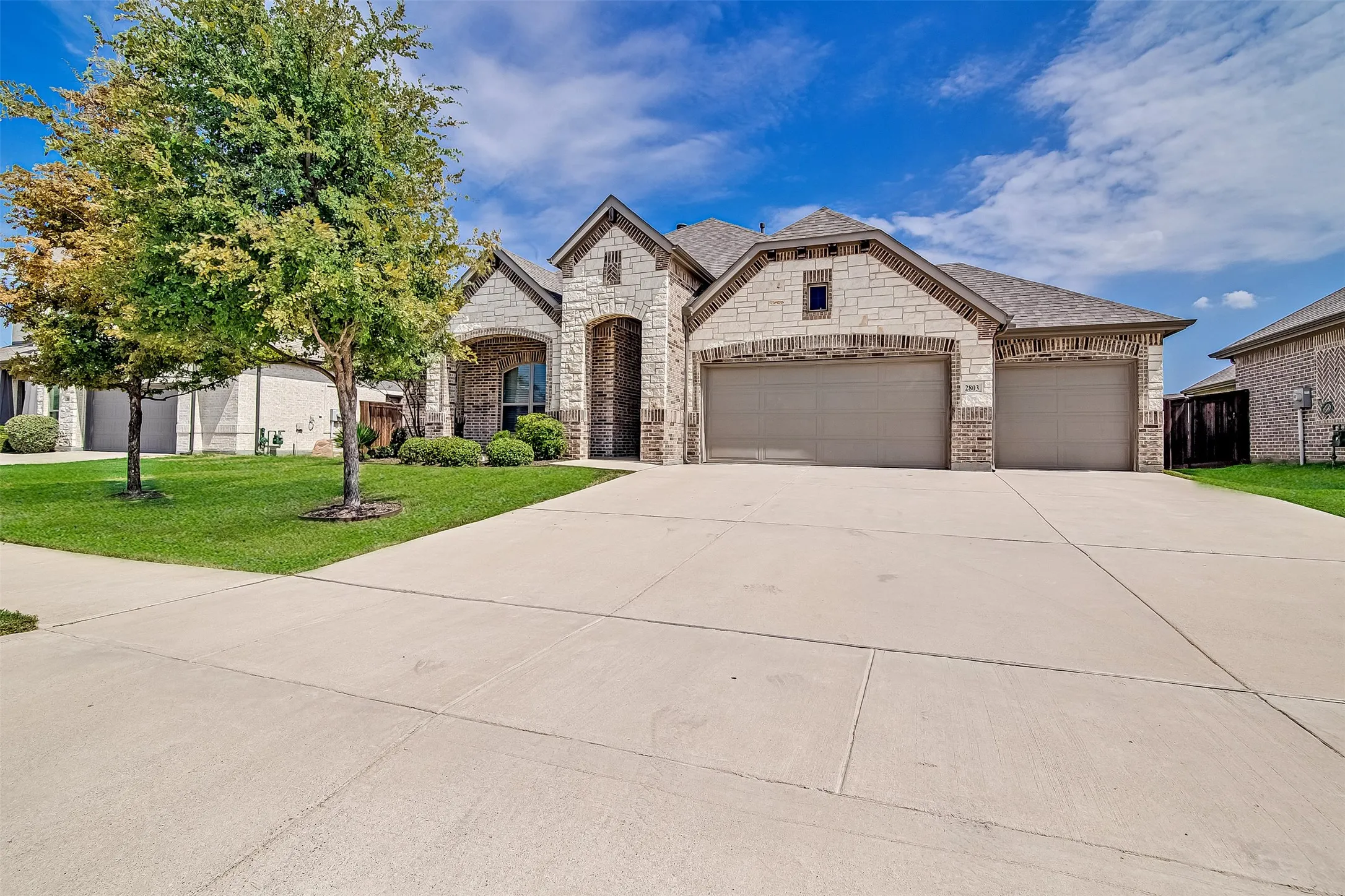 Stone and brick exterior featuring a multi-car garage, concrete driveway, and a well-maintained lawn