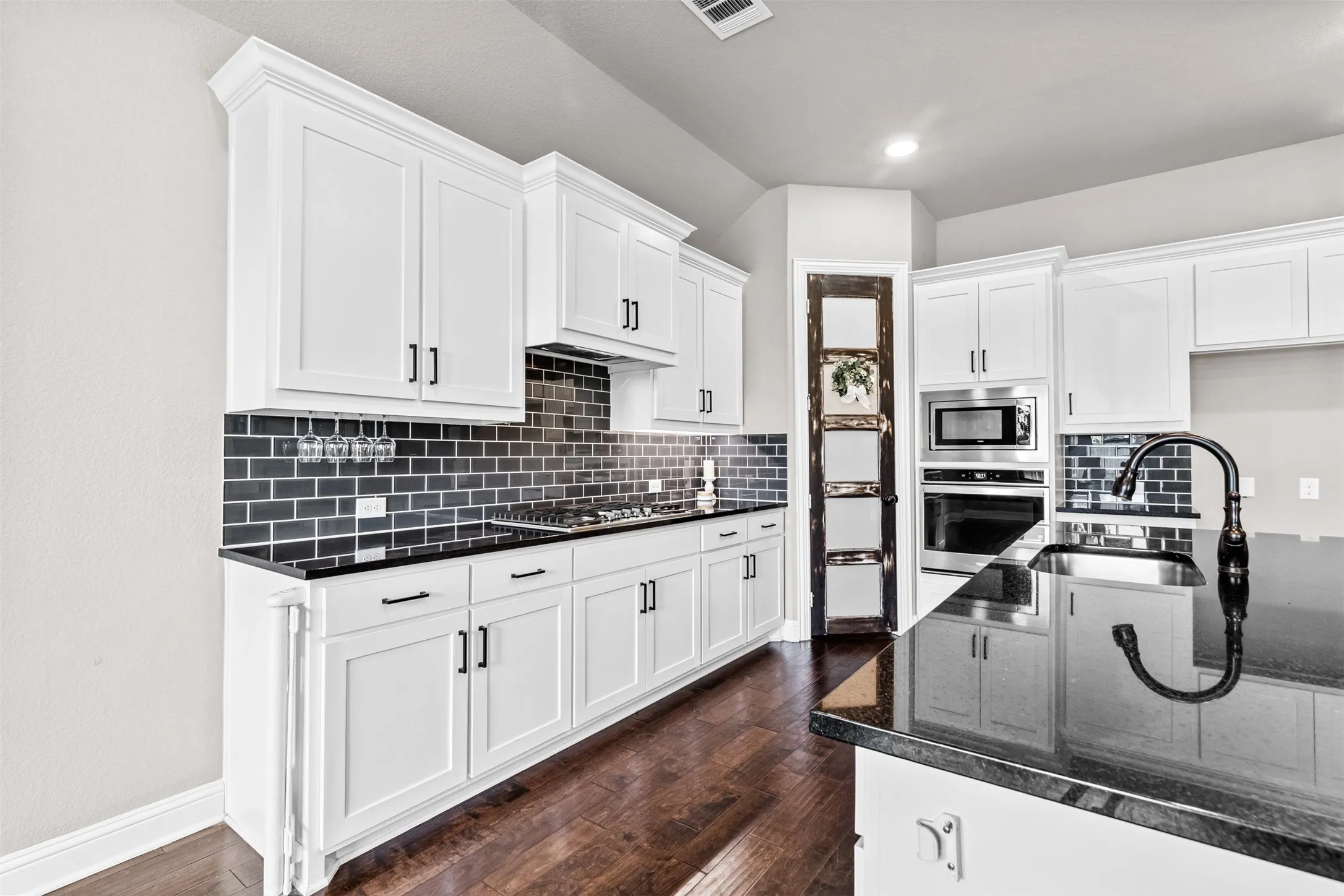 White shaker cabinetry, dark subway tile backsplash, black countertops, wood-finish flooring, and stainless steel appliances