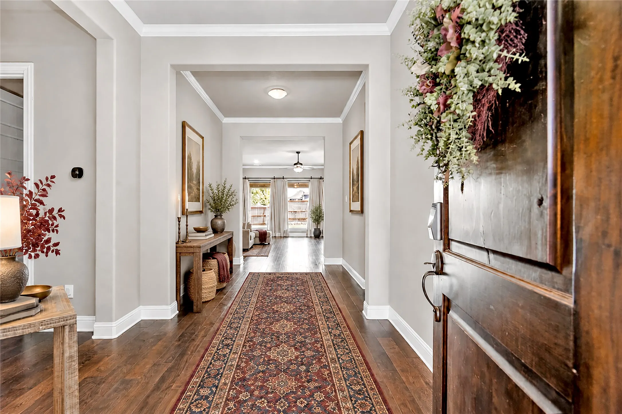 Rich wood-finish flooring, white crown molding, recessed lighting, and a dark wood entry door with dark bronze hardware. Virtual staged.