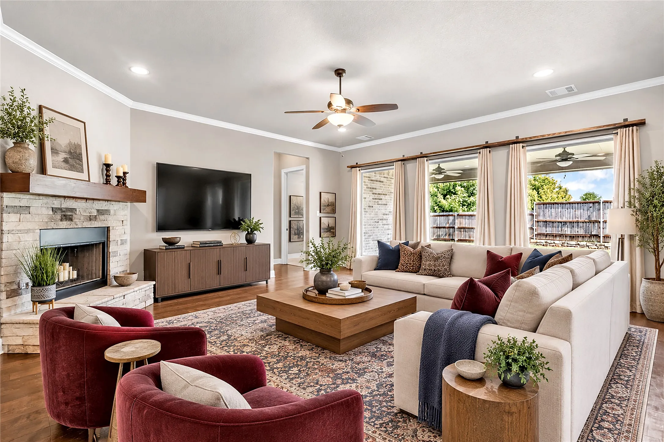 Stone-clad fireplace with a wood mantle, recessed lighting, crown molding, wood-finish flooring, and multiple large windows. Virtual staged.