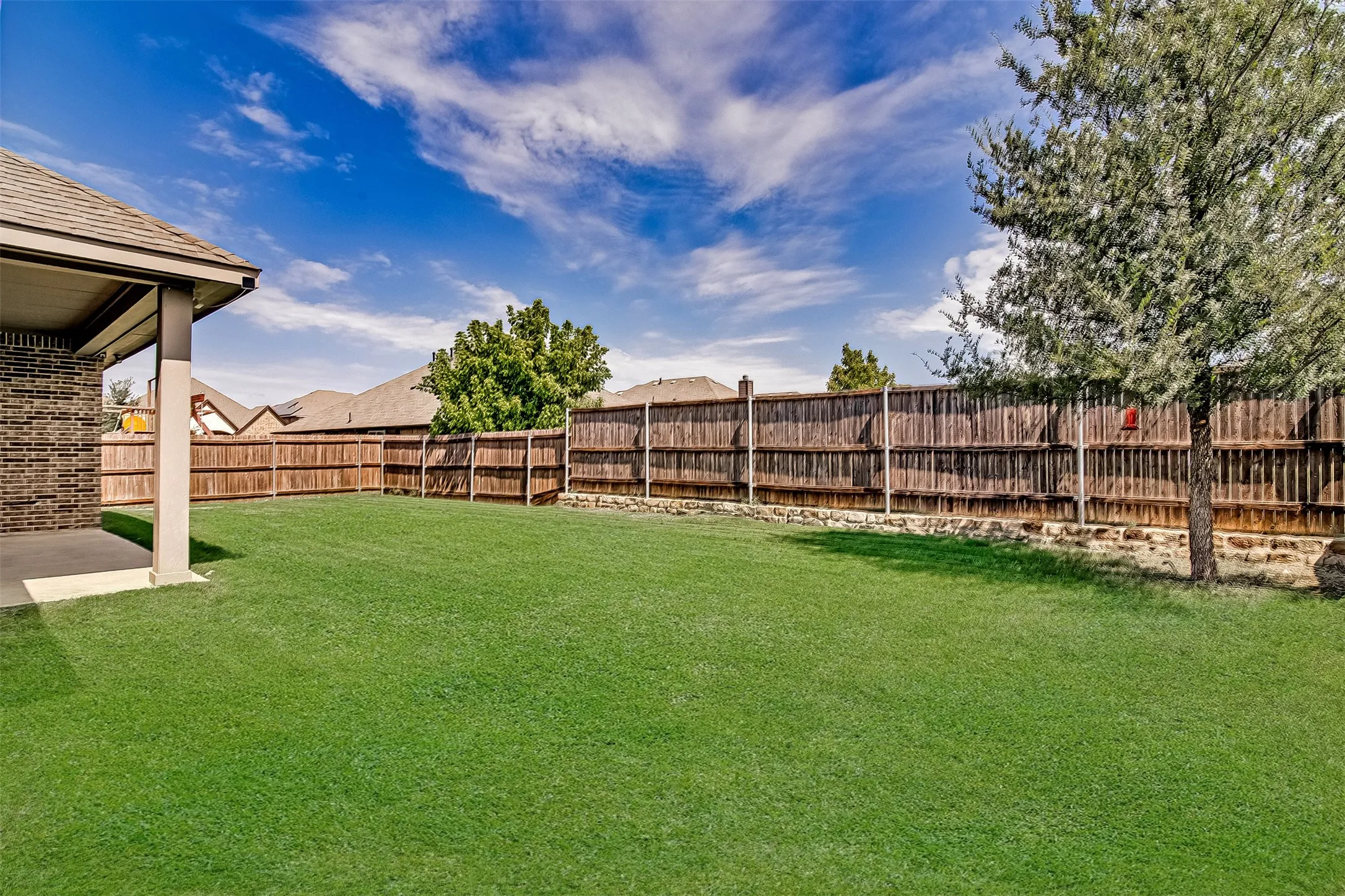 Expansive backyard featuring a lush lawn, privacy fencing, a covered patio, and mature landscaping