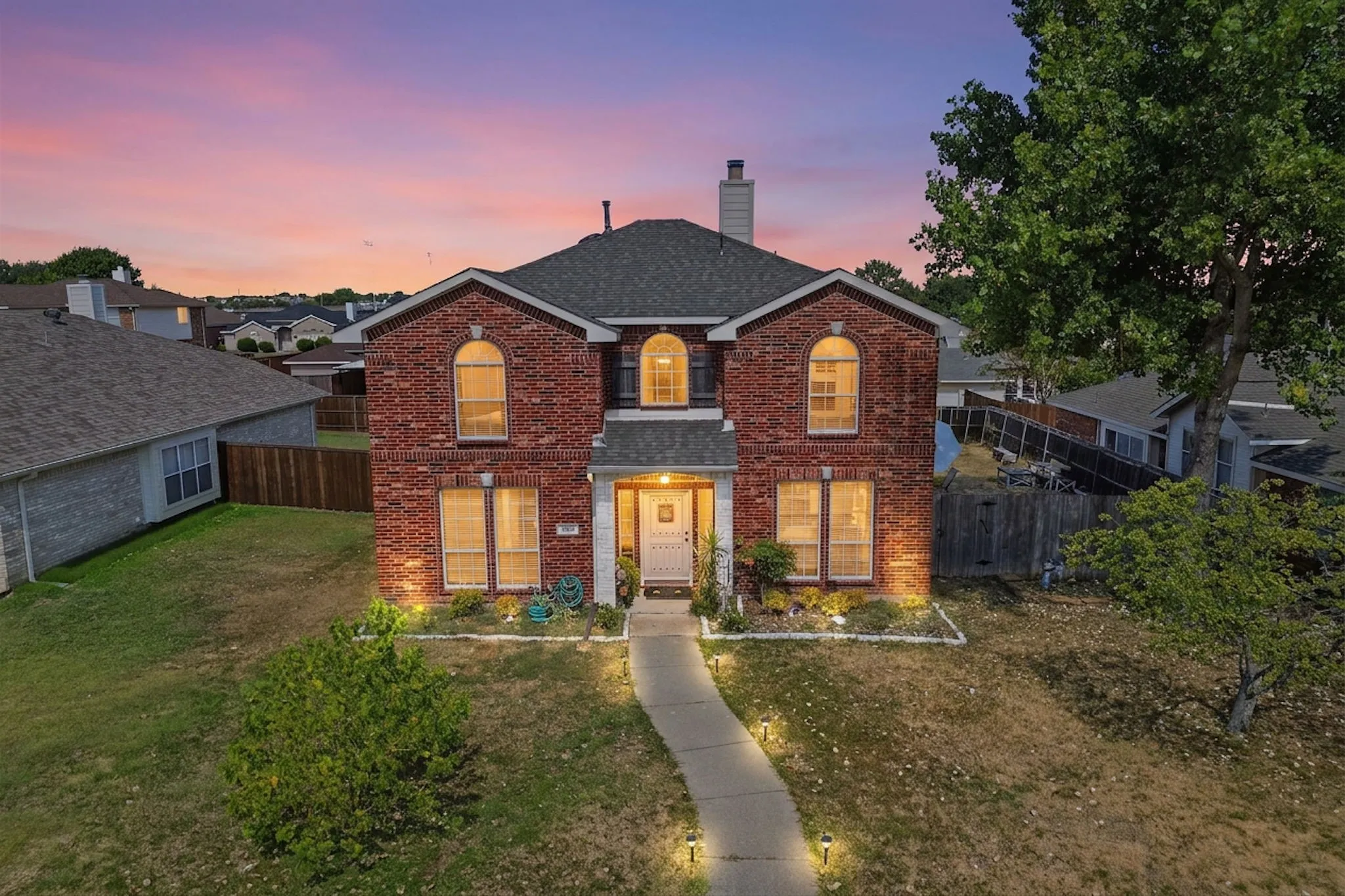 Red brick exterior with arched windows, a front walkway, and exterior lighting