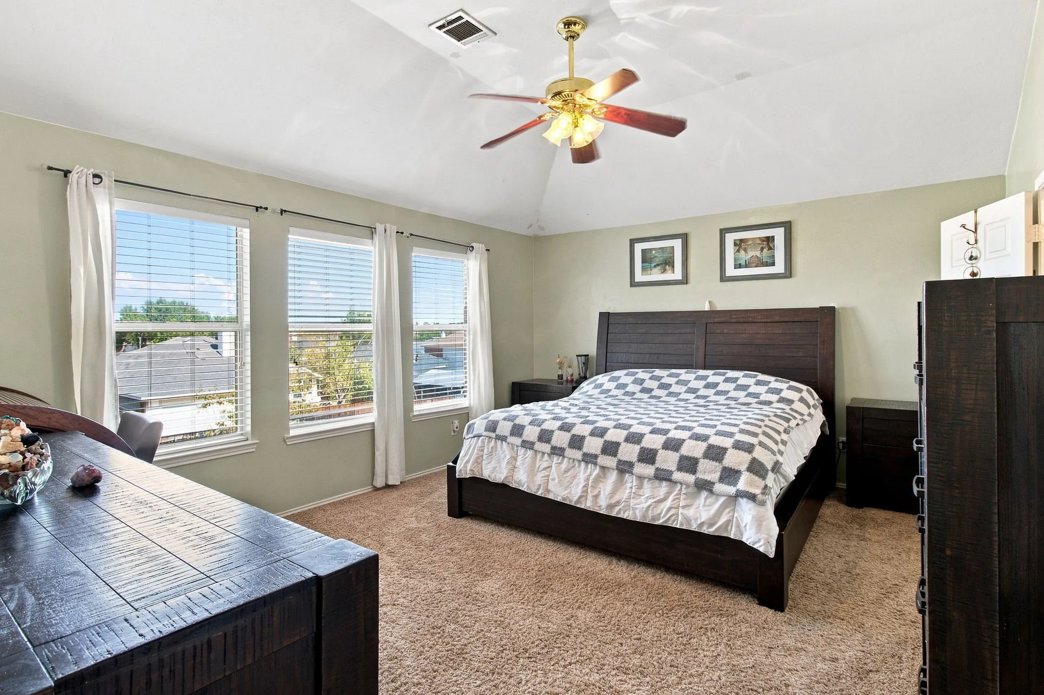 Vaulted ceiling with a ceiling fan, three large windows, textured carpet flooring, and neutral wall paint