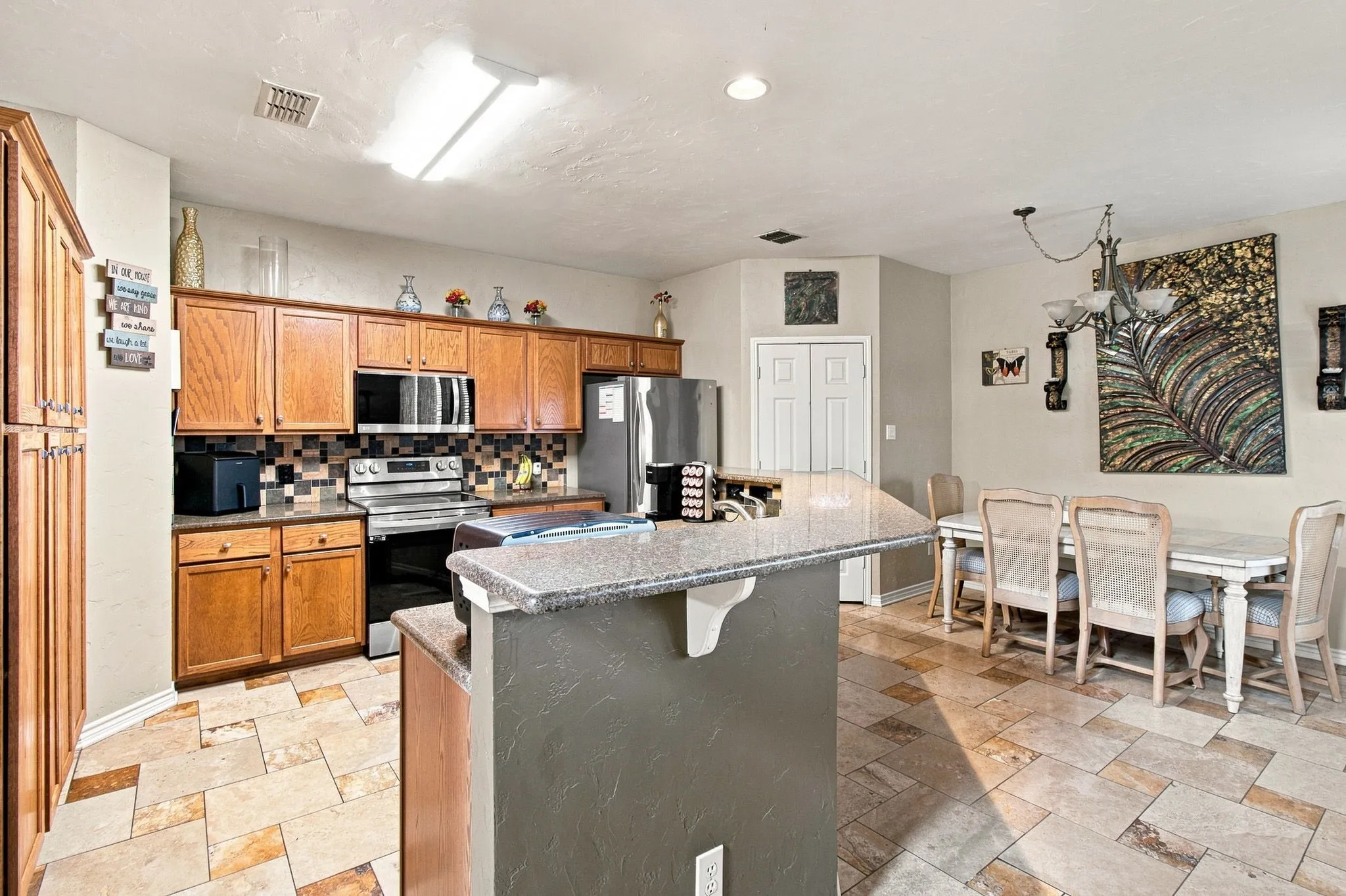 Kitchen featuring wood cabinetry, stainless steel appliances, a tiled backsplash, and stone-finish flooring