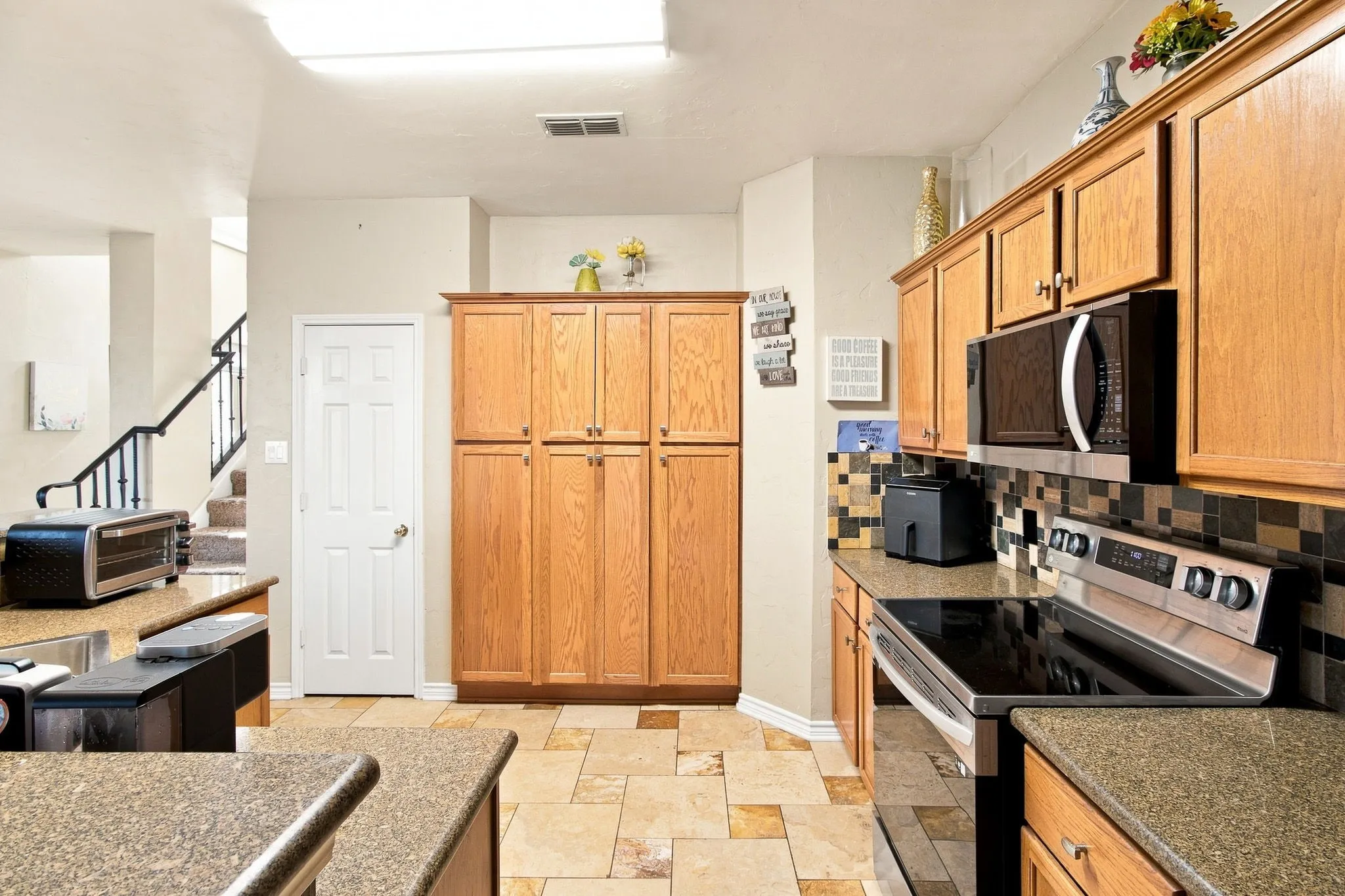 Kitchen featuring extensive wood cabinetry, tile flooring, solid surface countertops, stainless steel appliances, and a mosaic tile backsplash