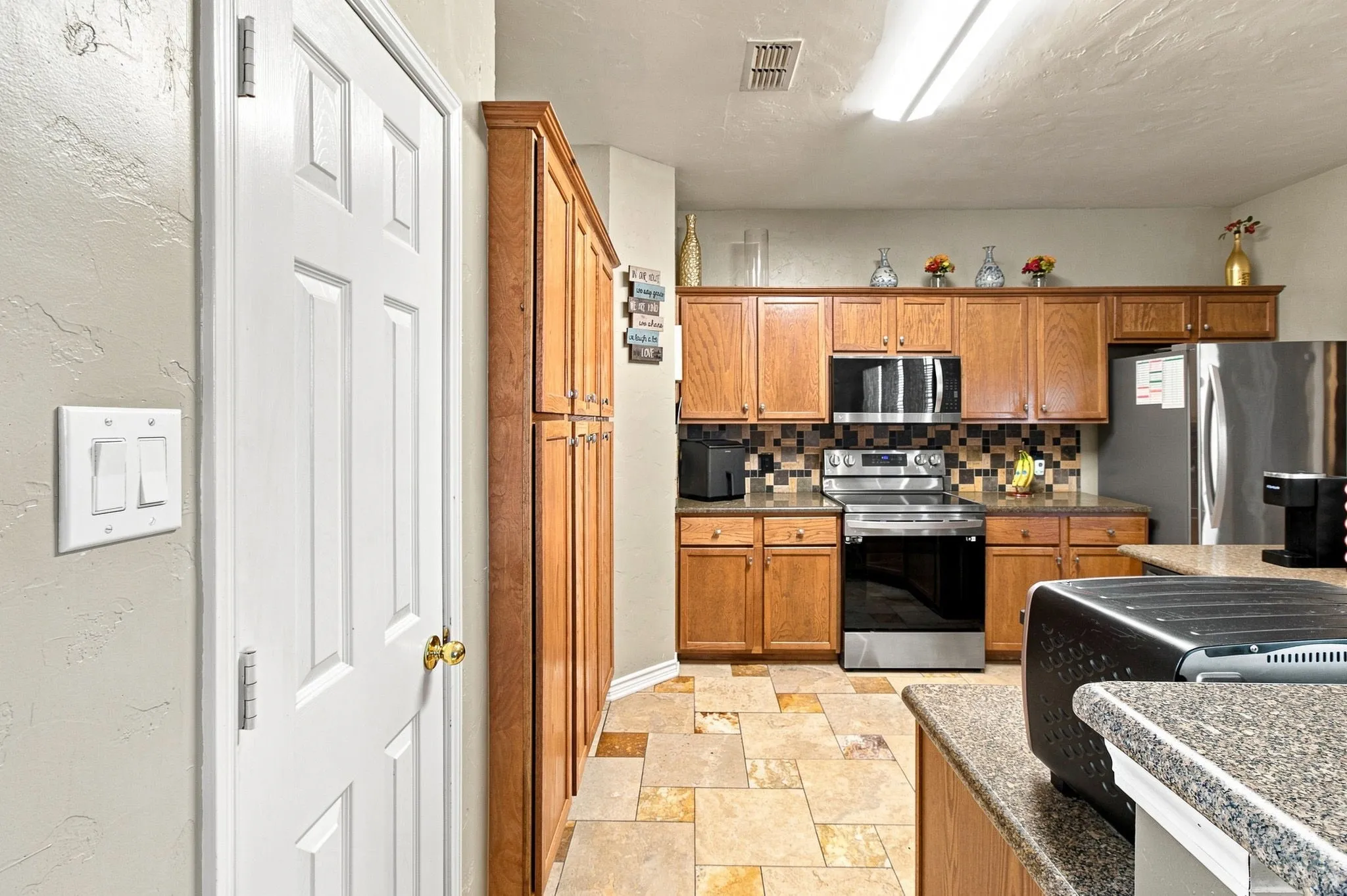 Kitchen featuring wood cabinetry, stainless steel appliances, mosaic tile backsplash, and patterned tile flooring