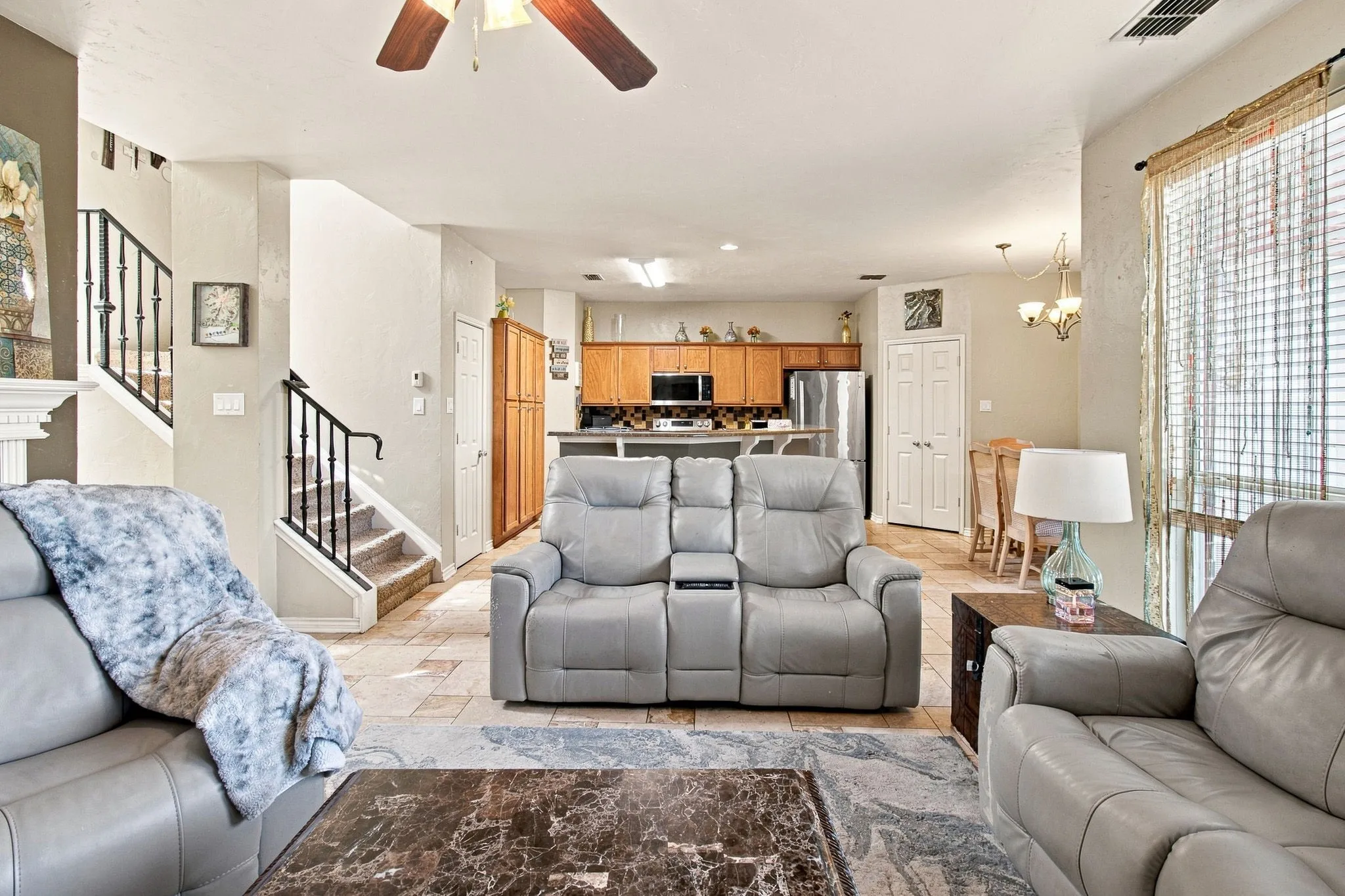 Open-concept living area featuring a ceiling fan, tile flooring, and a staircase with wrought iron balusters