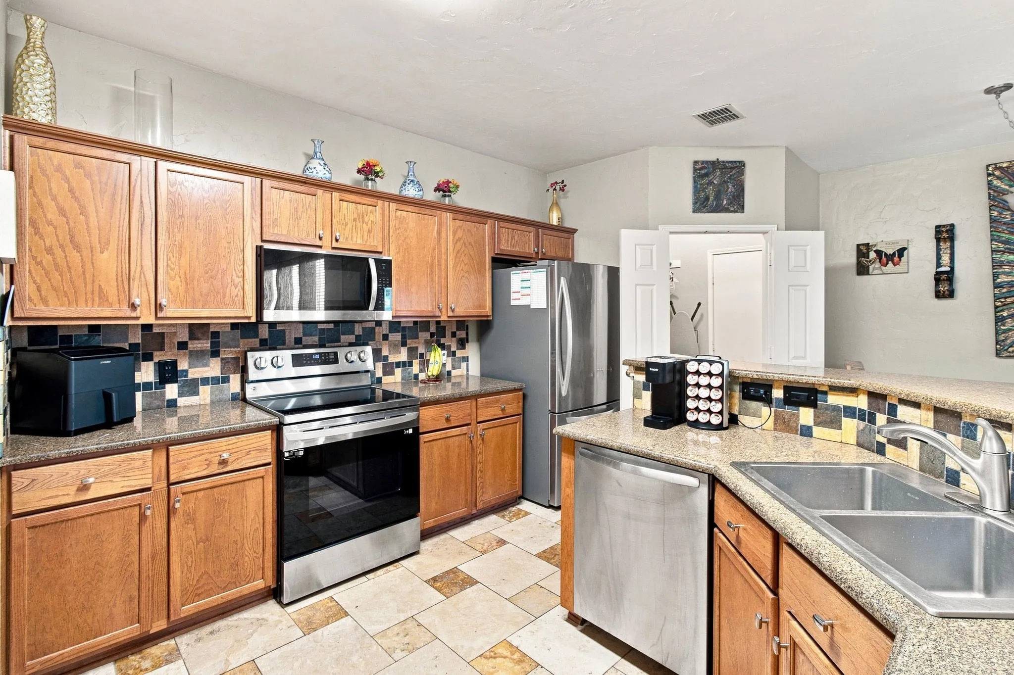 Wood-finish cabinetry, stainless steel appliances, tiled flooring, granite-style countertops, and a tiled backsplash